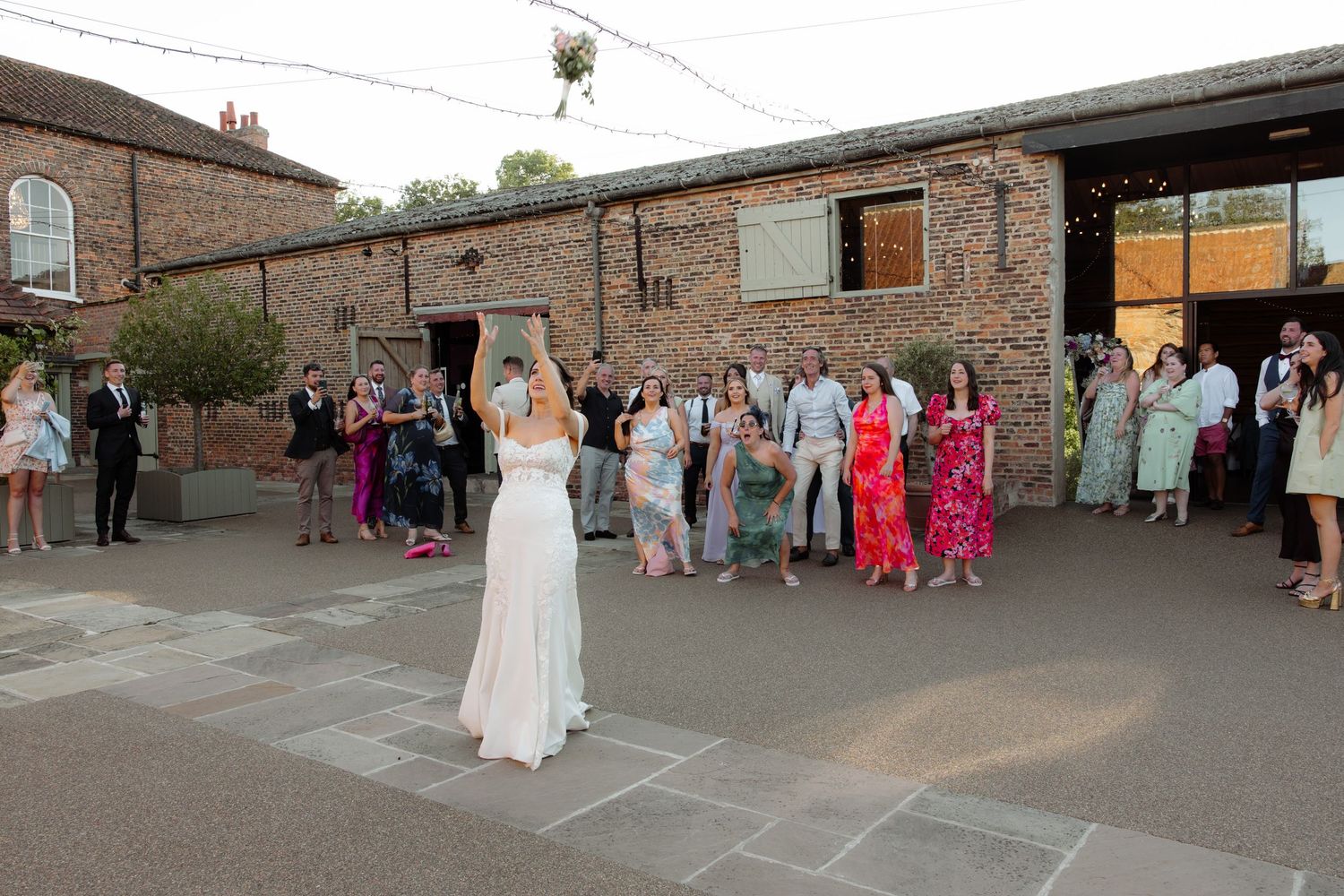 Wedding guests gather outside a rustic brick venue during a celebration.
