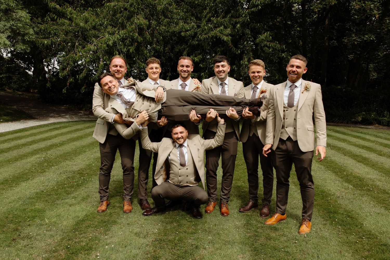 A wedding party strikes a fun pose together on a manicured lawn during a summer celebration.