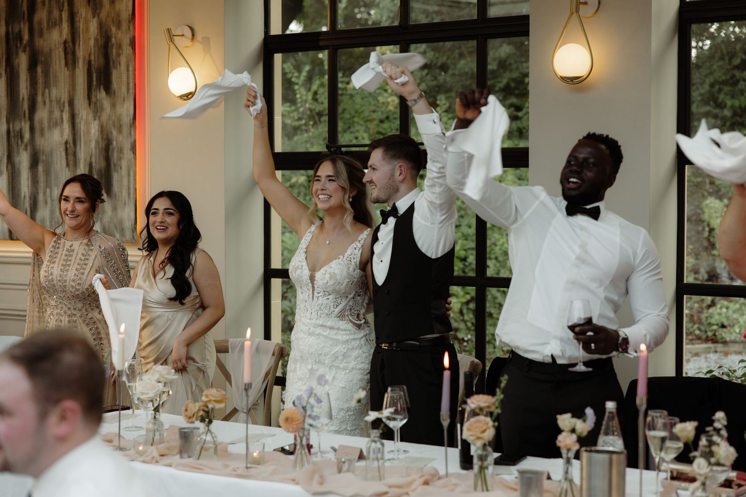 Wedding guests raise their glasses in celebration during a reception toast at an elegant indoor venue.