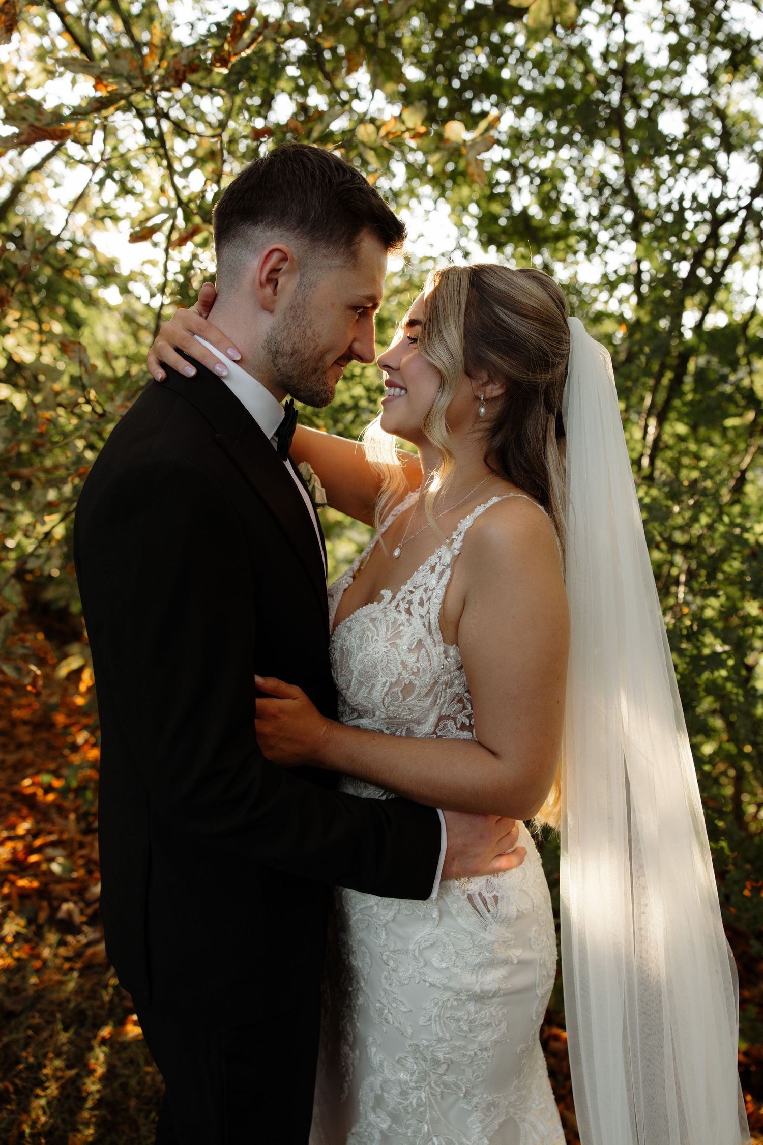 A couple shares joyful laughter during their outdoor wedding photoshoot among trees at golden hour.