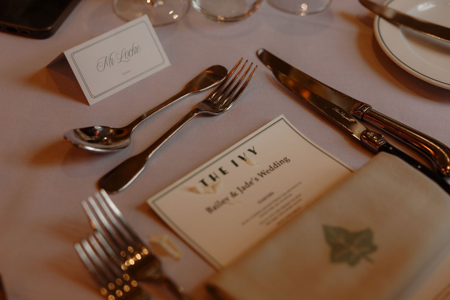 Elegant place settings at a formal dinner table with name cards, wine glasses, and silver cutlery in warm lighting.