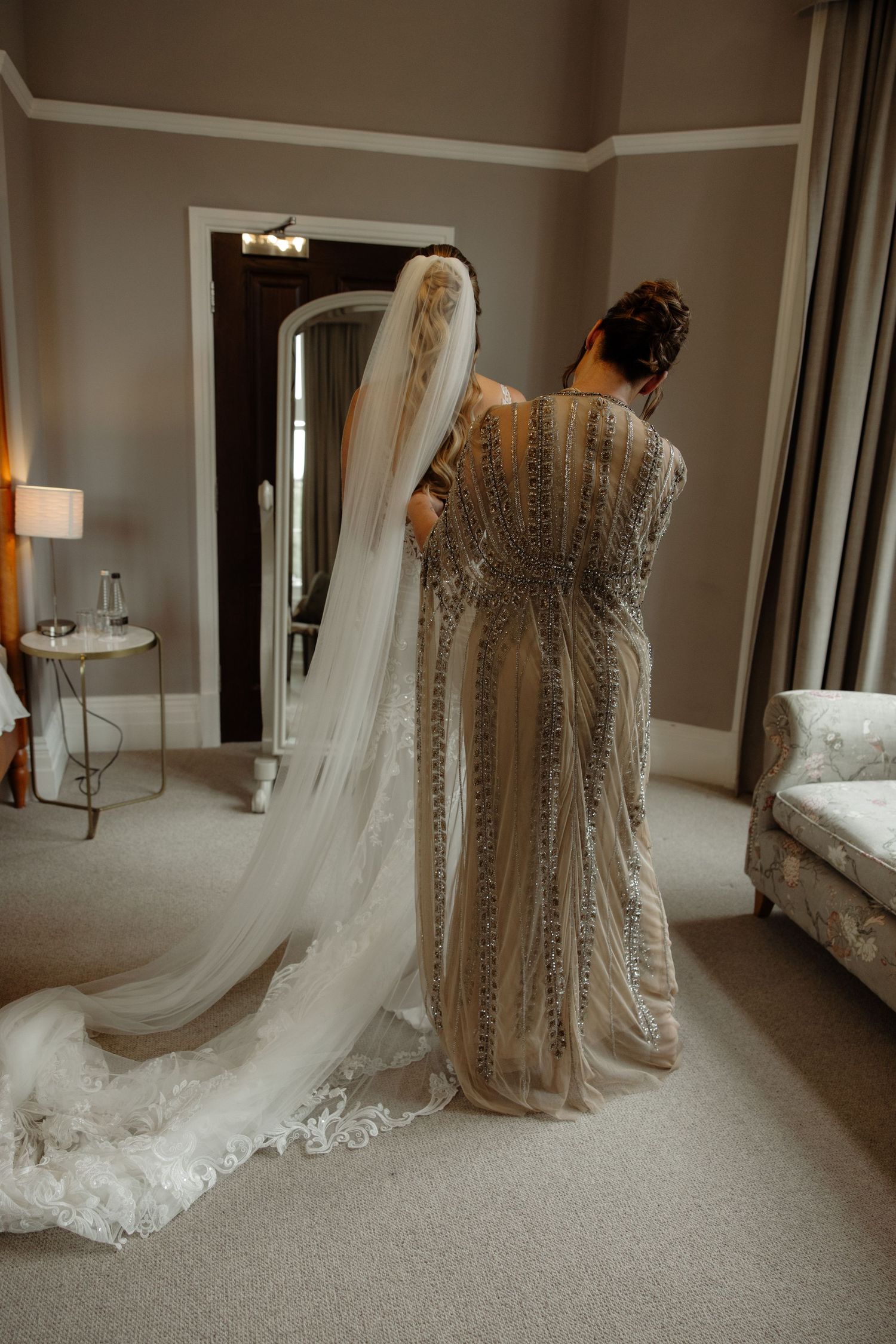 A detailed lace wedding dress and flowing veil displayed in a neutral-toned room with soft lighting.
