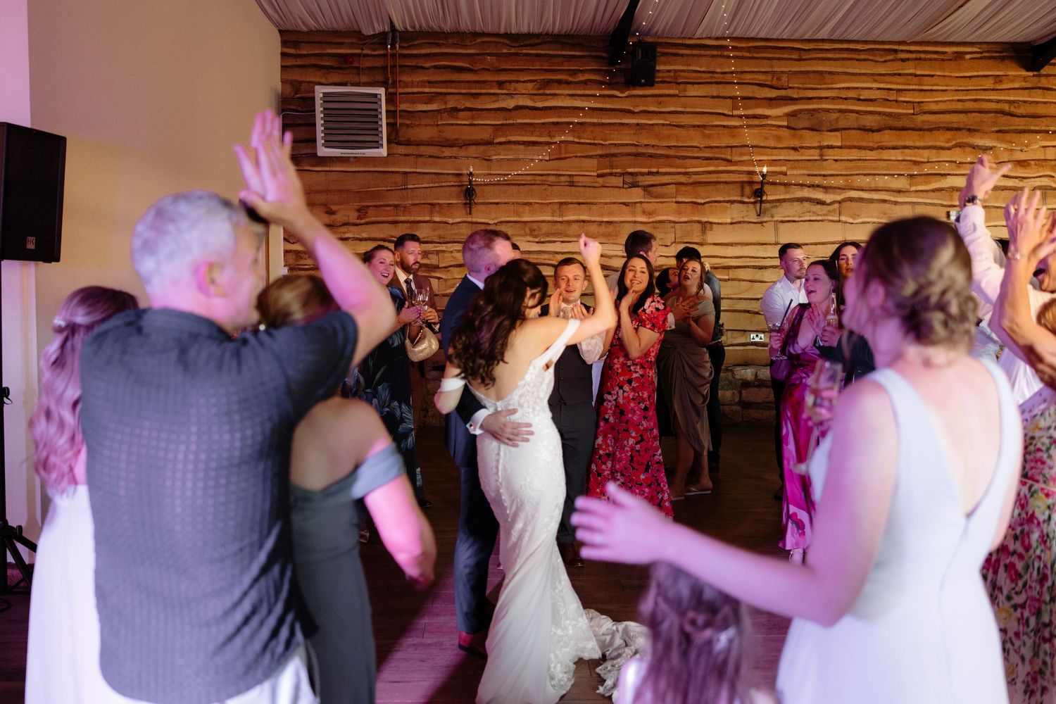 Wedding guests dance and celebrate on a wooden dance floor at a rustic venue.