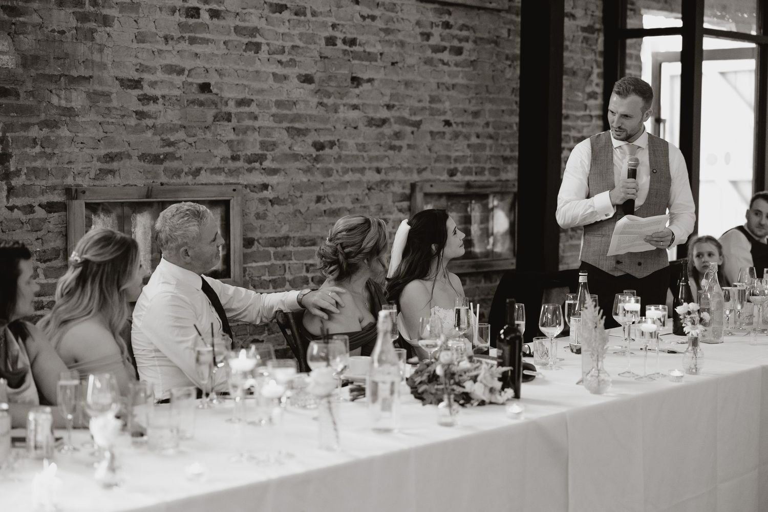 A panoramic view of people dining at a long table in a rustic brick-walled restaurant setting.