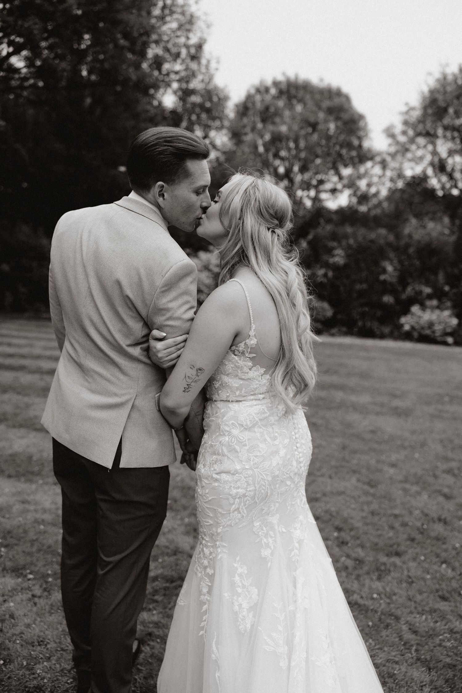 Black and white photo of a romantic wedding moment with couple embracing outdoors in a garden setting.