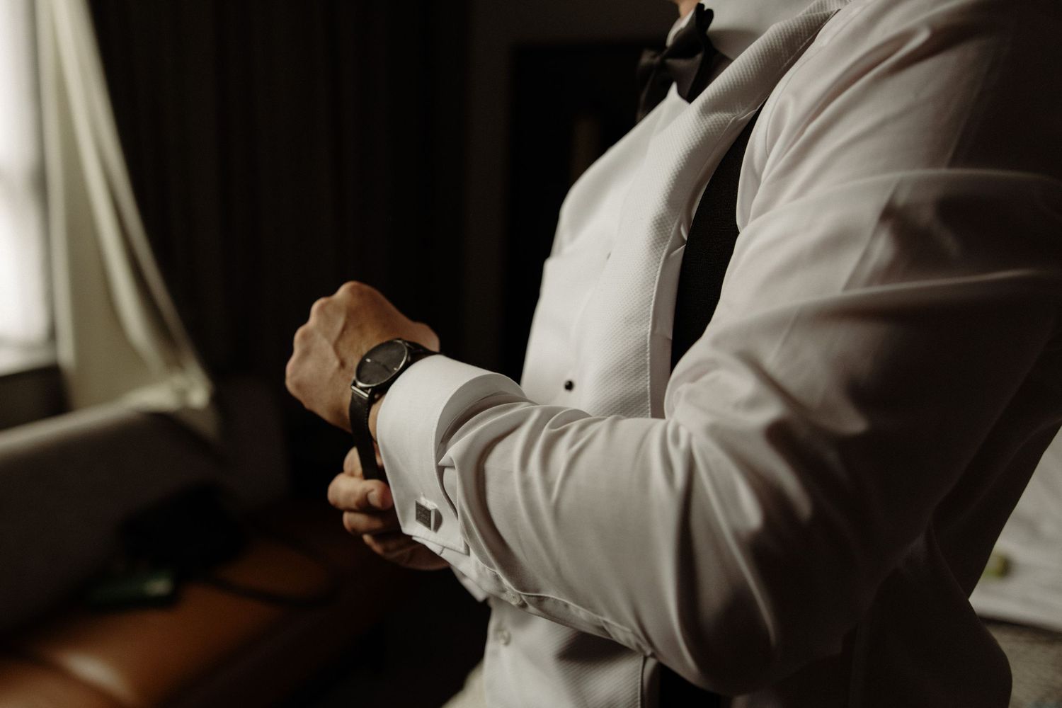 A person in a white dress shirt adjusts their cuff links while getting ready.
