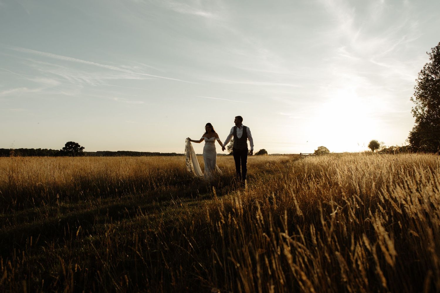 Silhouettes of a couple walking hand in hand through a golden wheat field at sunset.