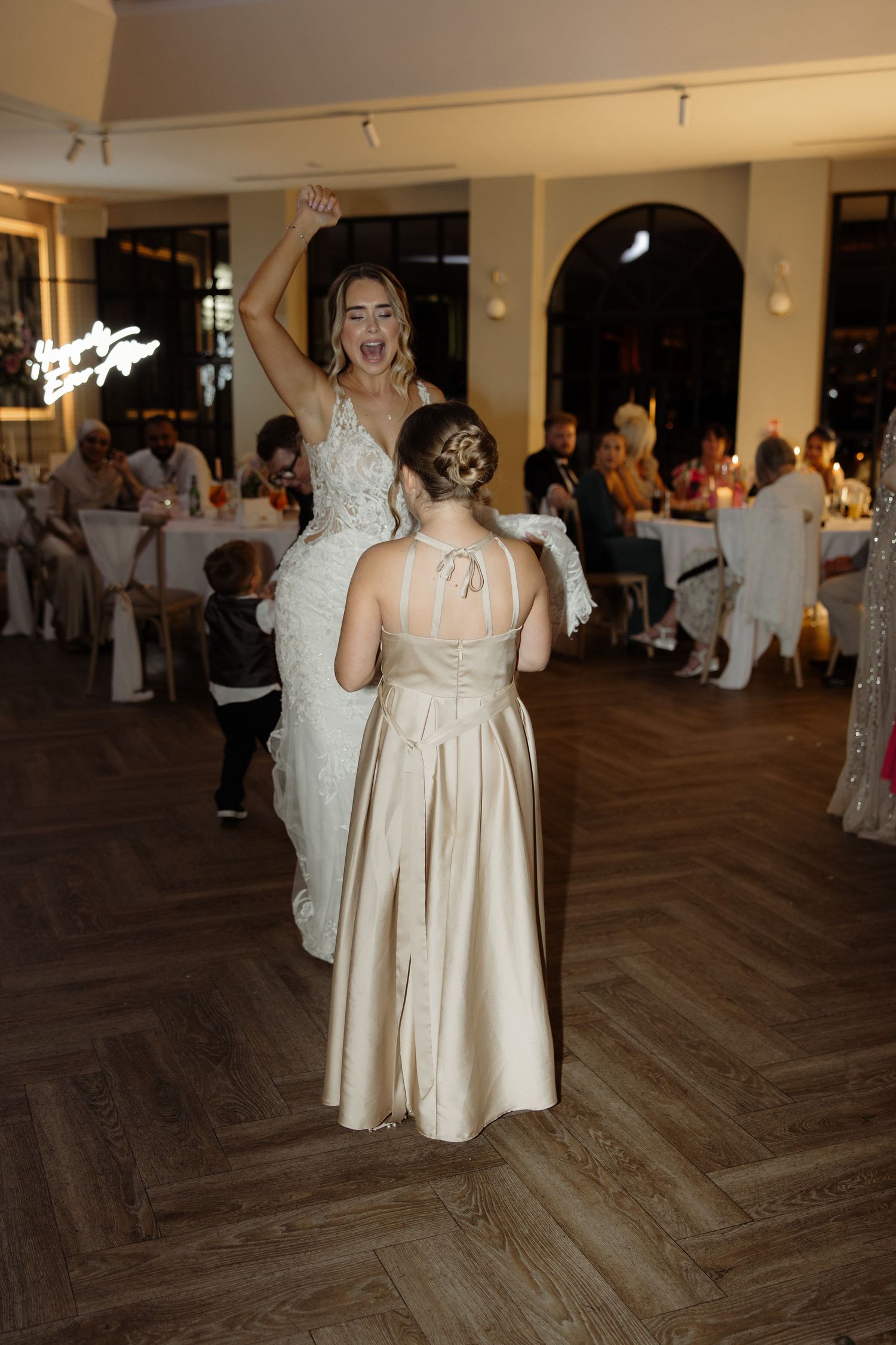 People dancing and celebrating at a wedding reception in a venue with wooden floors and white decor.
