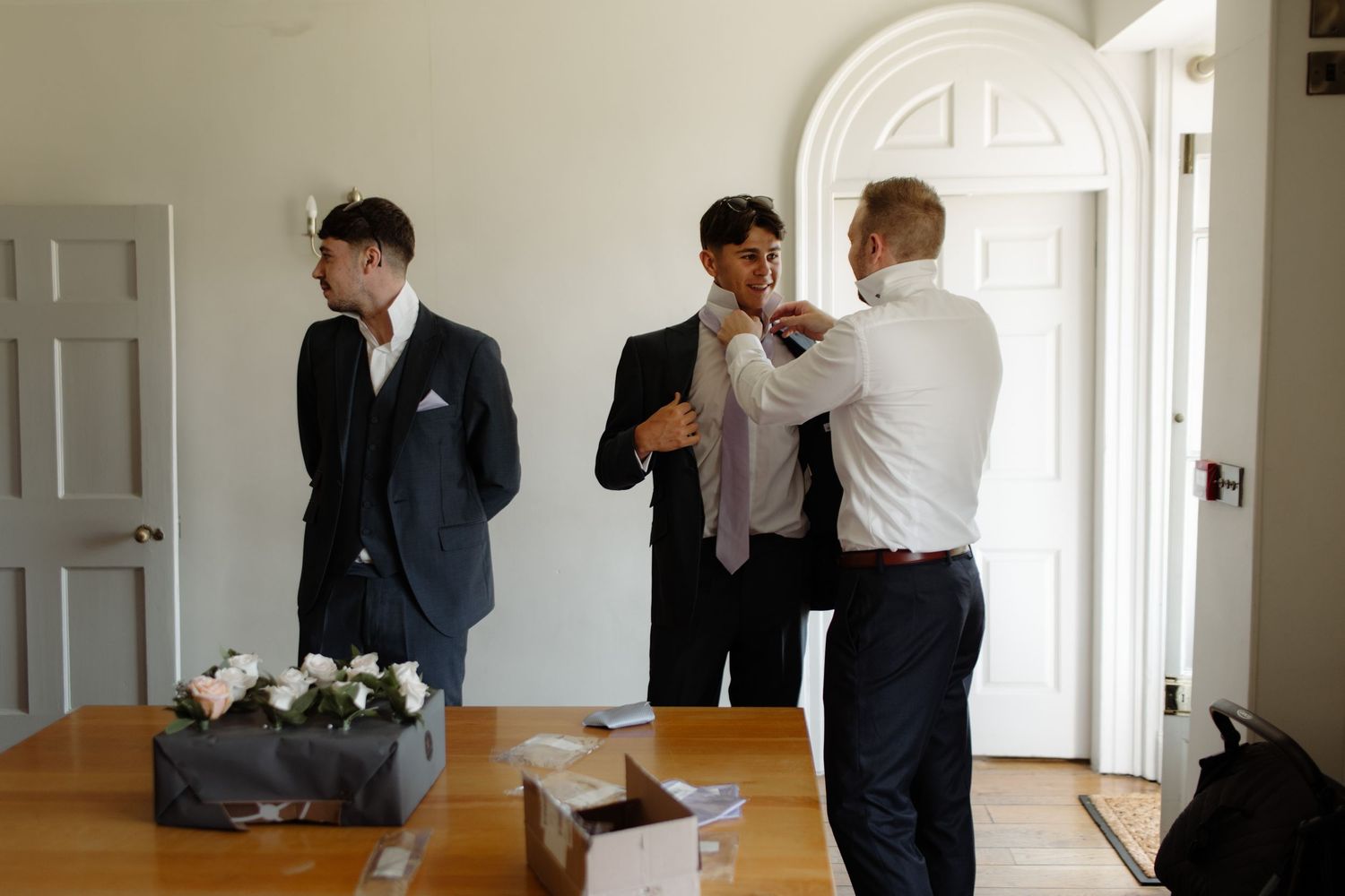 A sequence of black and white photos showing a groom getting ready and putting on his suit for a wedding ceremony.
