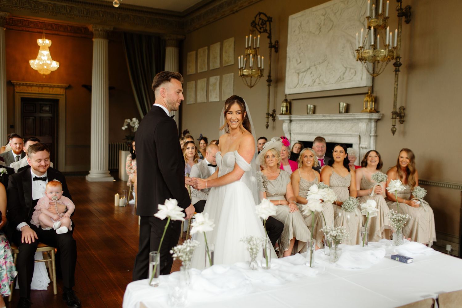 Wedding guests celebrate during a reception at an elegant venue with crystal chandeliers and classic decor.