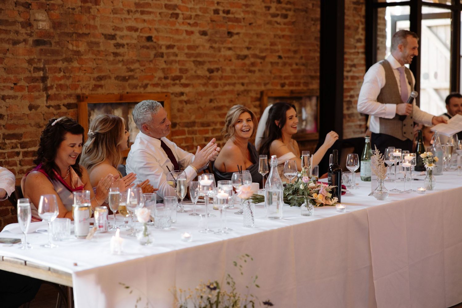 Wedding guests seated at long tables in a rustic brick venue during an elegant reception dinner.
