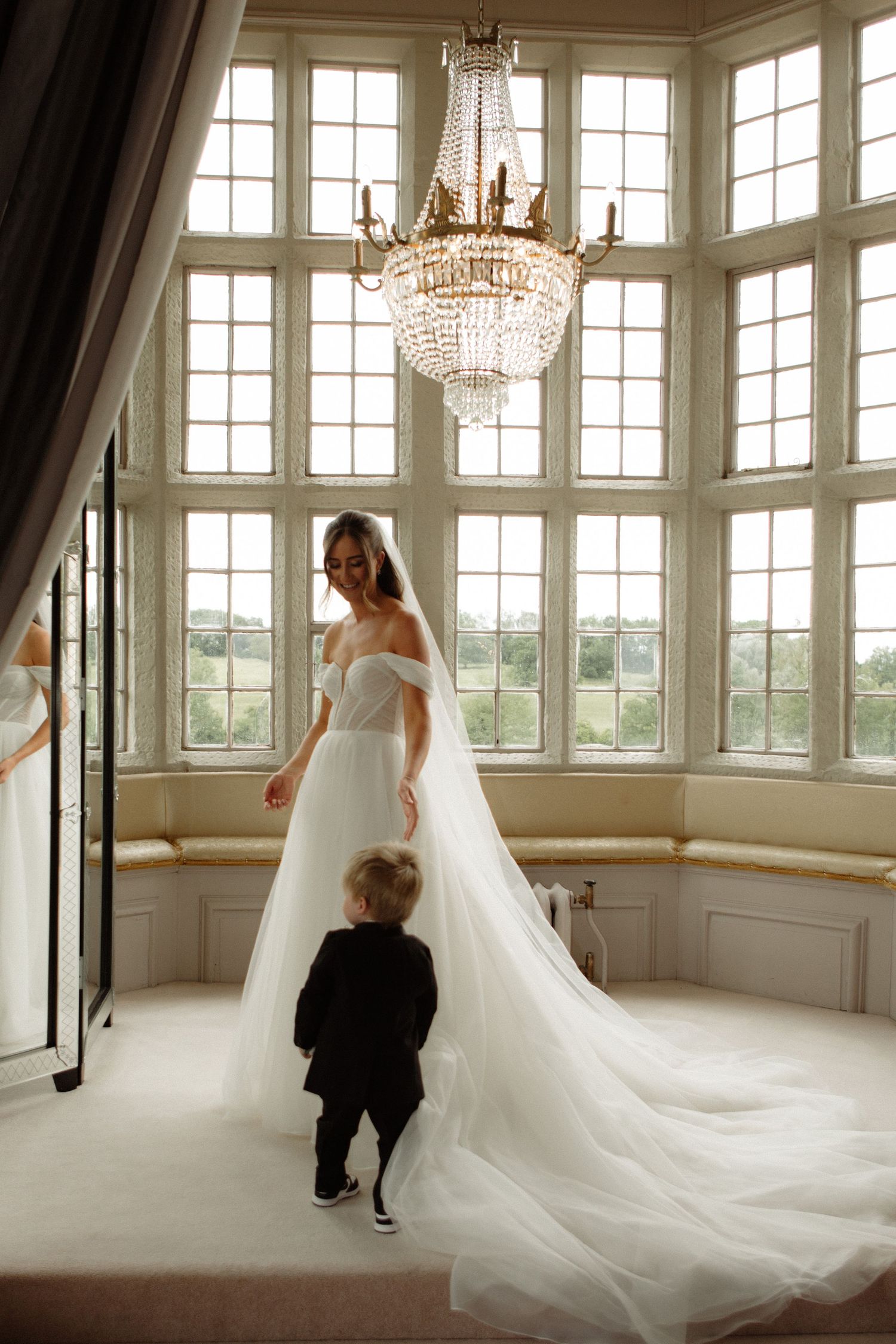 White wedding dress with flowing cathedral-length train in elegant sunlit room with crystal chandeliers.