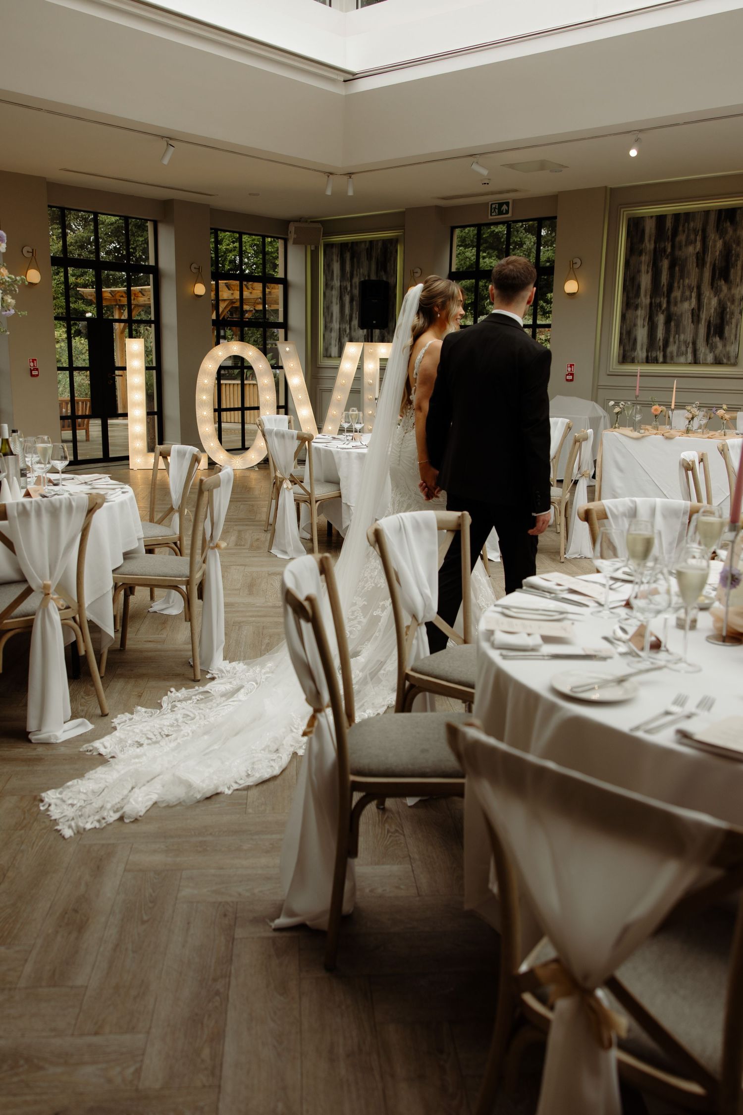 Elegant wedding reception venue with white-clothed tables, chairs, and flowing bridal gown details in natural light.