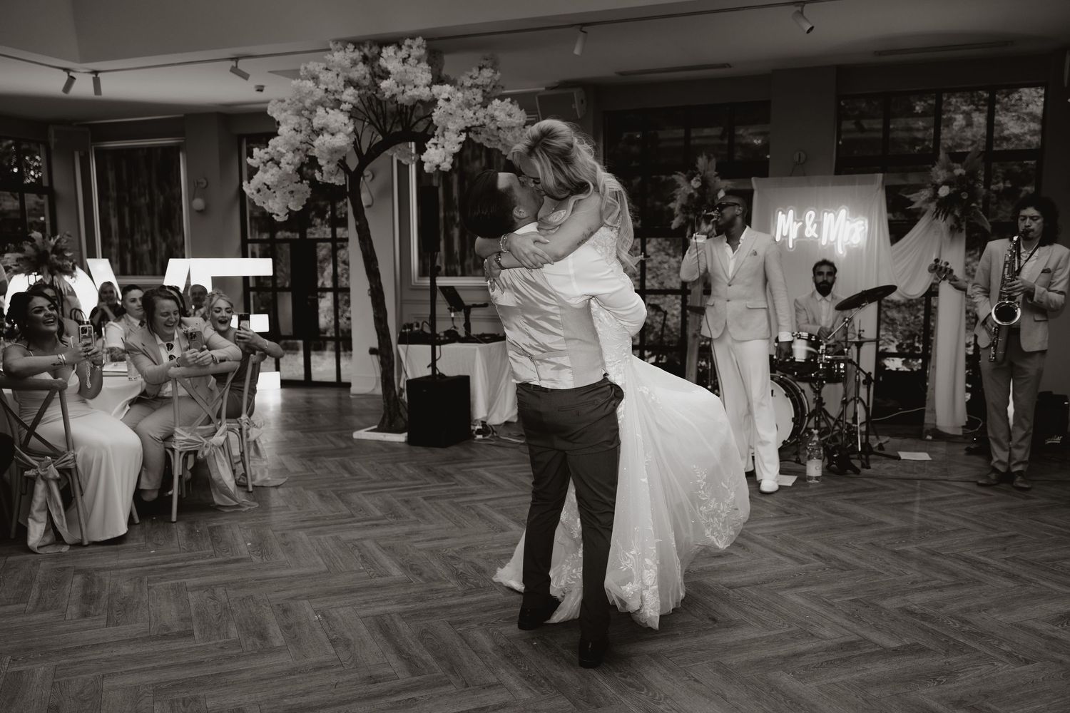 A couple shares their first dance at a wedding reception on a parquet dance floor while guests look on from the sidelines.