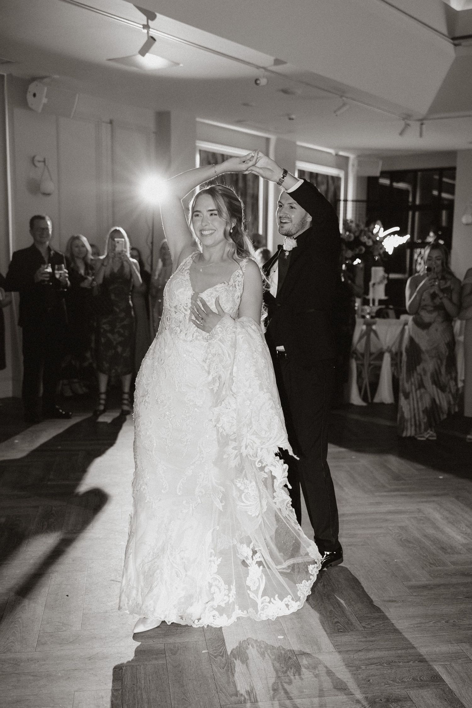 A couple shares their first dance at a wedding reception while guests look on in a brightly lit indoor venue.