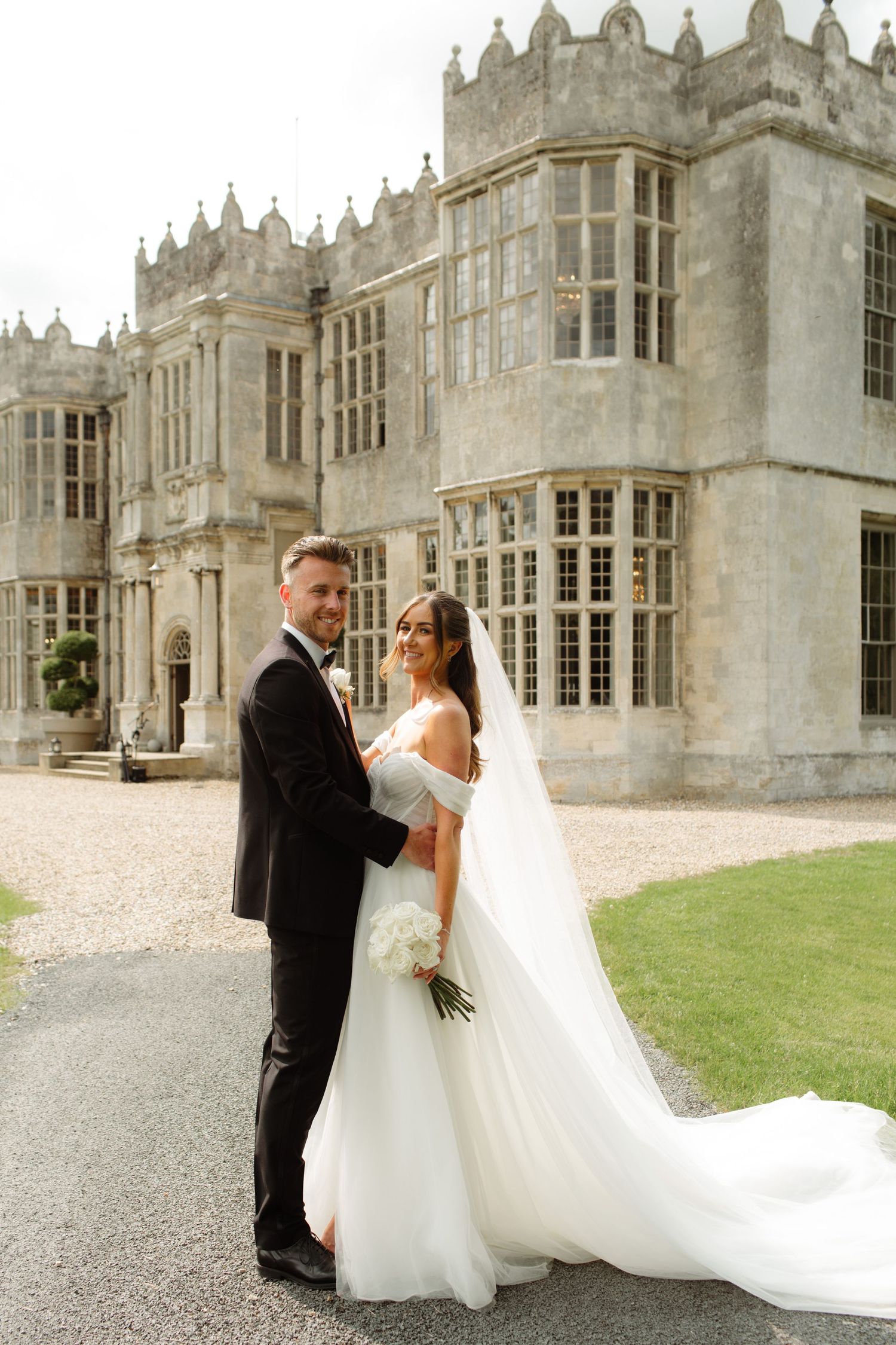 A bride and groom share romantic moments in front of a grand gothic stone mansion during their wedding photoshoot.