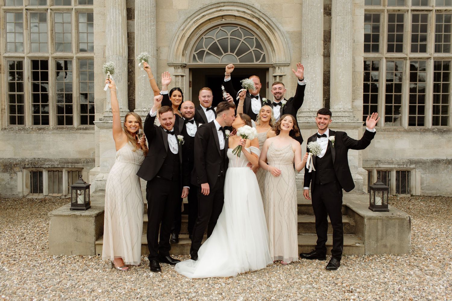 Wedding party celebrates and poses together on stone steps of an elegant historic building during a special day.