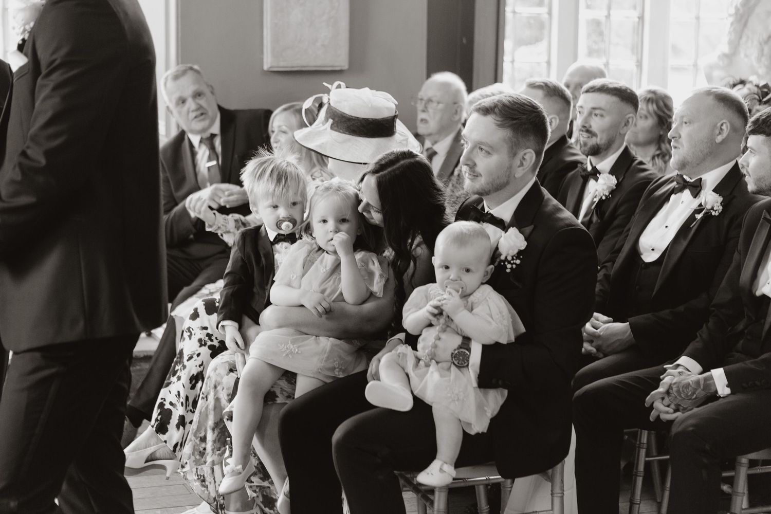 Wedding guests share emotional laughter and applause during a special moment at a reception in black and white.