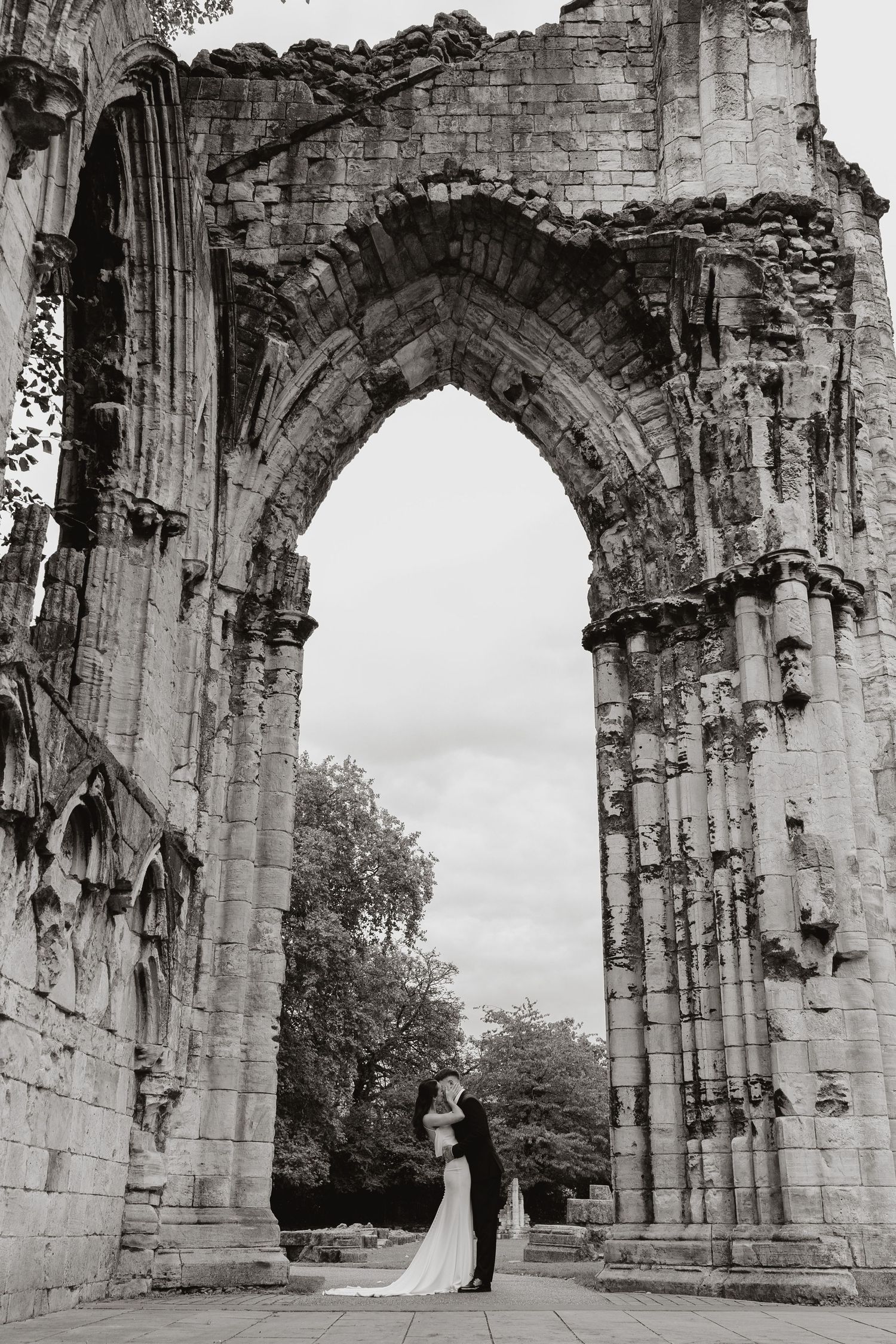 Ancient stone arches of St Mary's Abbey ruins stand against cloudy sky in York, England.
