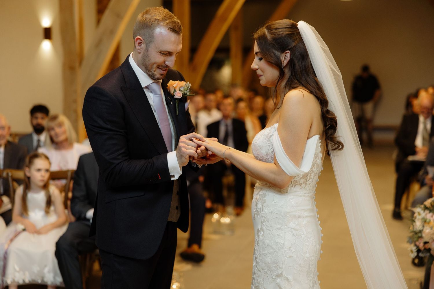 A couple shares their first dance as newlyweds in a warmly lit ballroom surrounded by wedding guests.