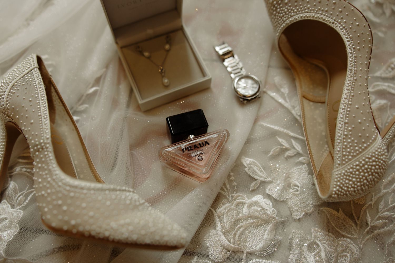 An elegant arrangement of wedding accessories including white lace, pearls, shoes, and satin details spread on a surface.