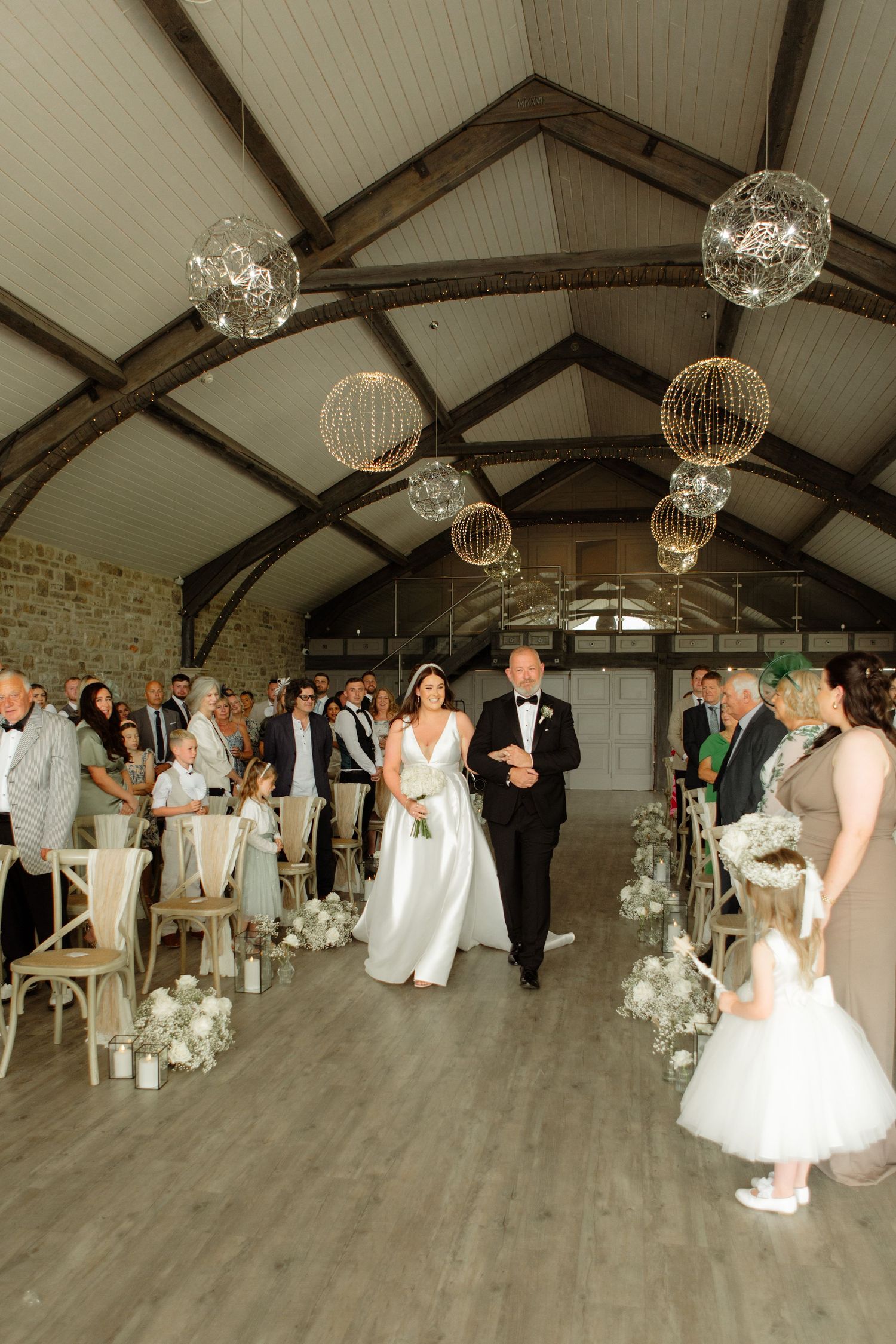 Wedding guests dance in a rustic barn venue decorated with elegant crystal chandeliers and exposed wooden beams.