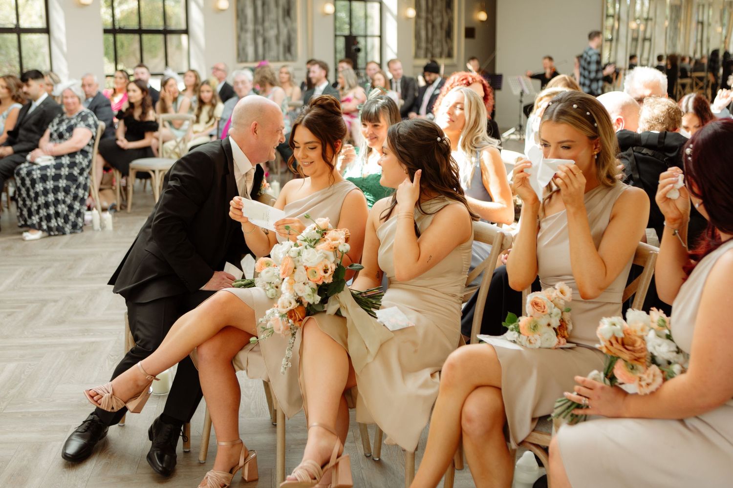 Wedding party members sit together in formal attire on outdoor steps during a summer celebration.