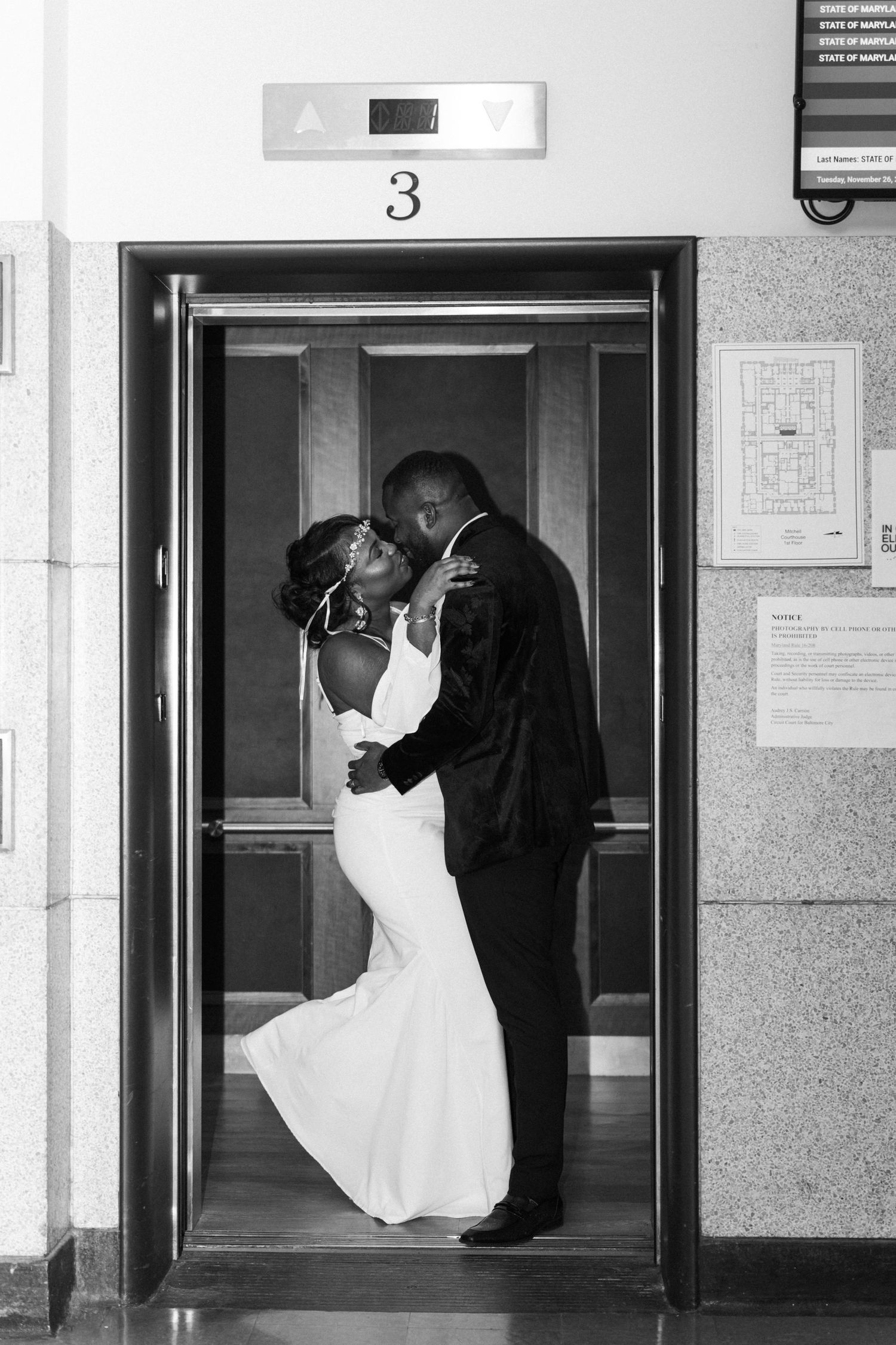 Black and white photo of a bride and groom sharing a kiss inside an elevator.