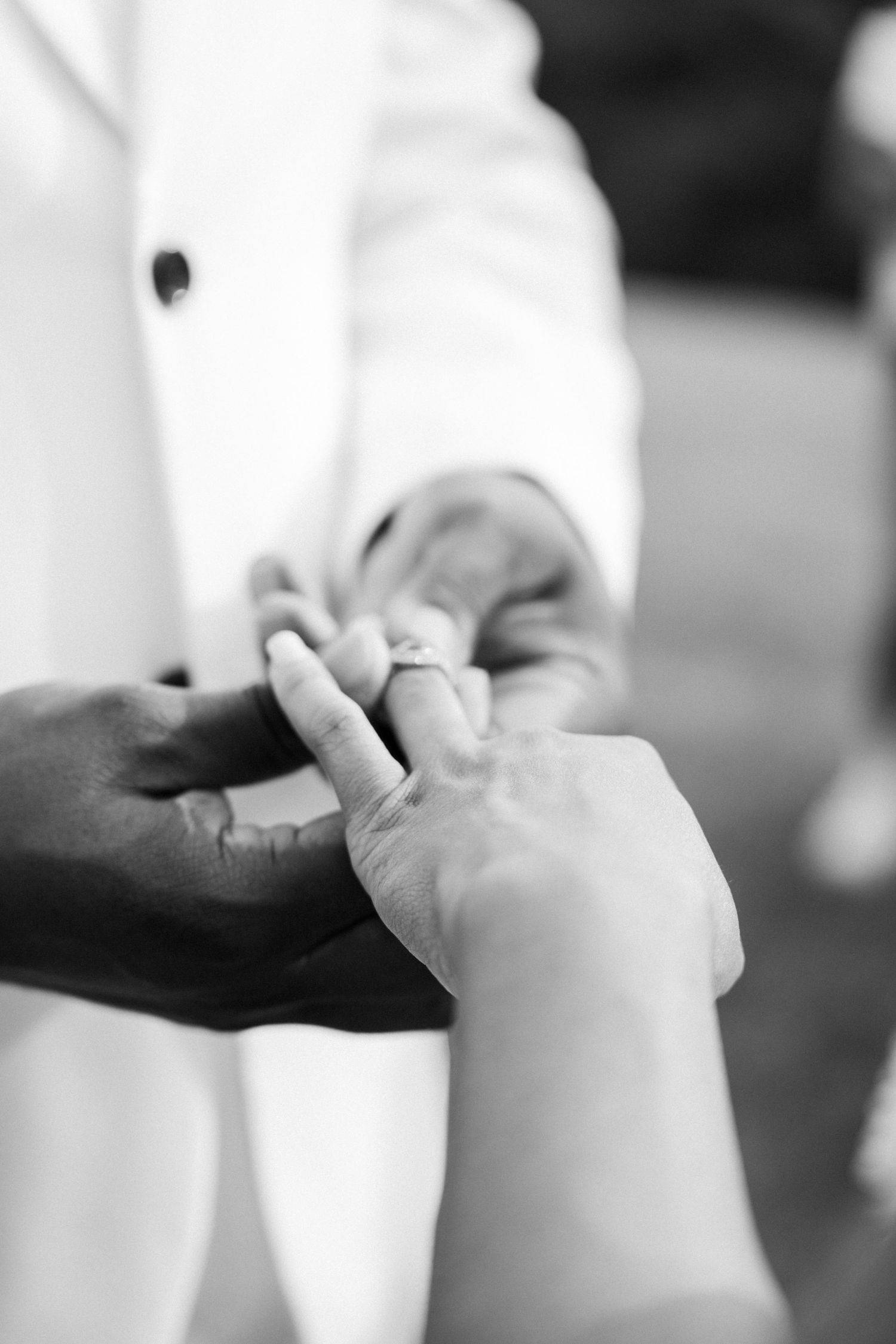 Black and white photo of an interracial couple exchanging wedding rings during a ceremony.