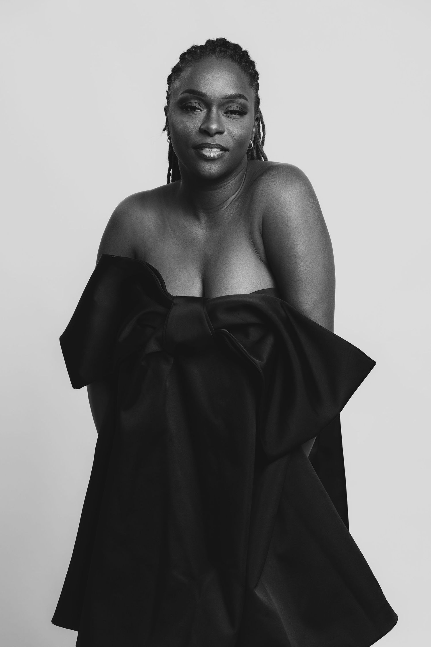 Black and white portrait of a woman in a strapless black bow gown, posing confidently against a light background.
