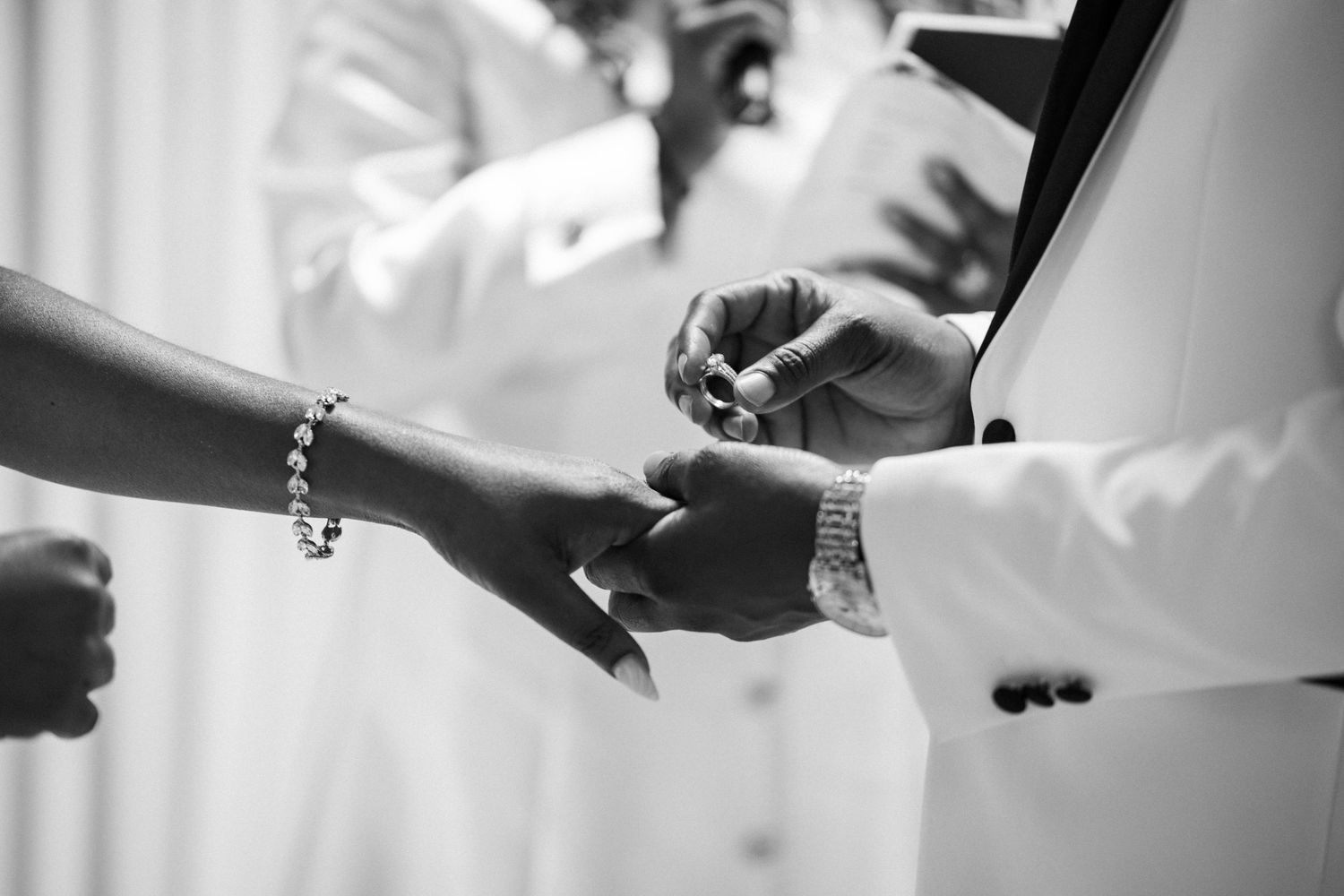 Black and white photo of a groom placing a wedding ring on the bride's finger during a ceremony.
