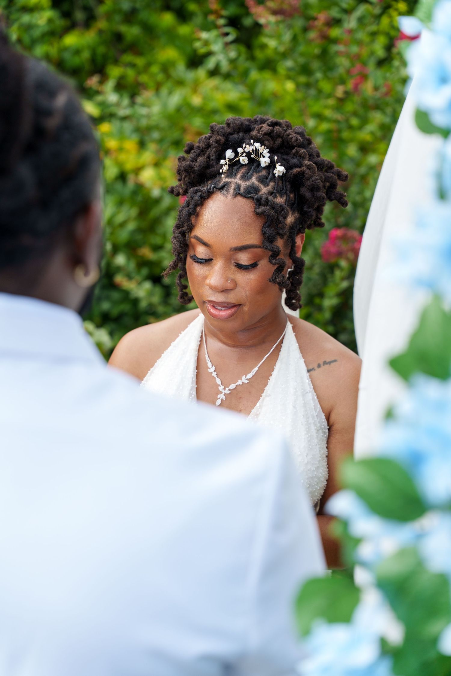 Black bride in white halter gown with pearl hair accessories and diamond necklace during outdoor wedding ceremony.