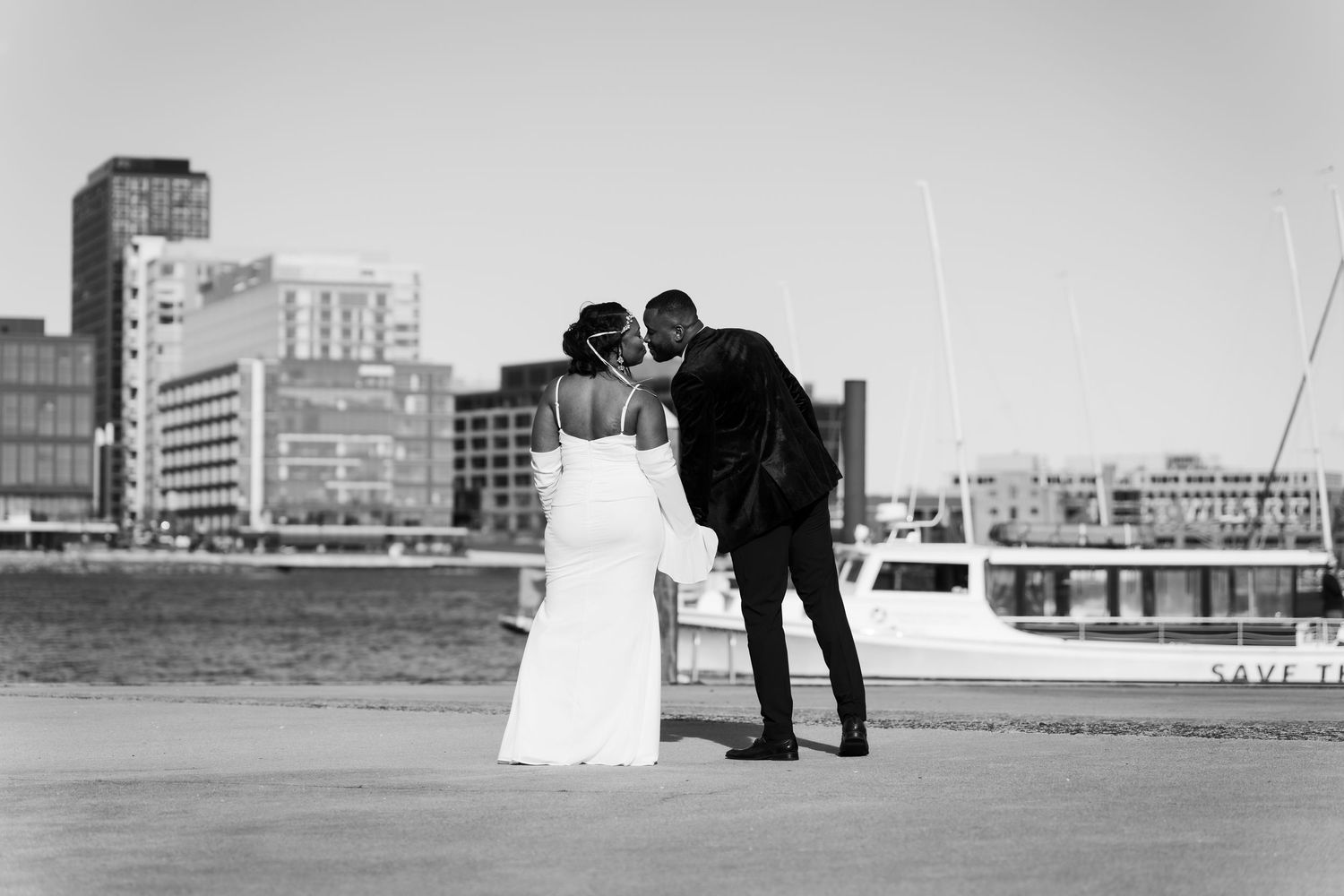 Couple sharing a kiss by waterfront with city skyline in background.
