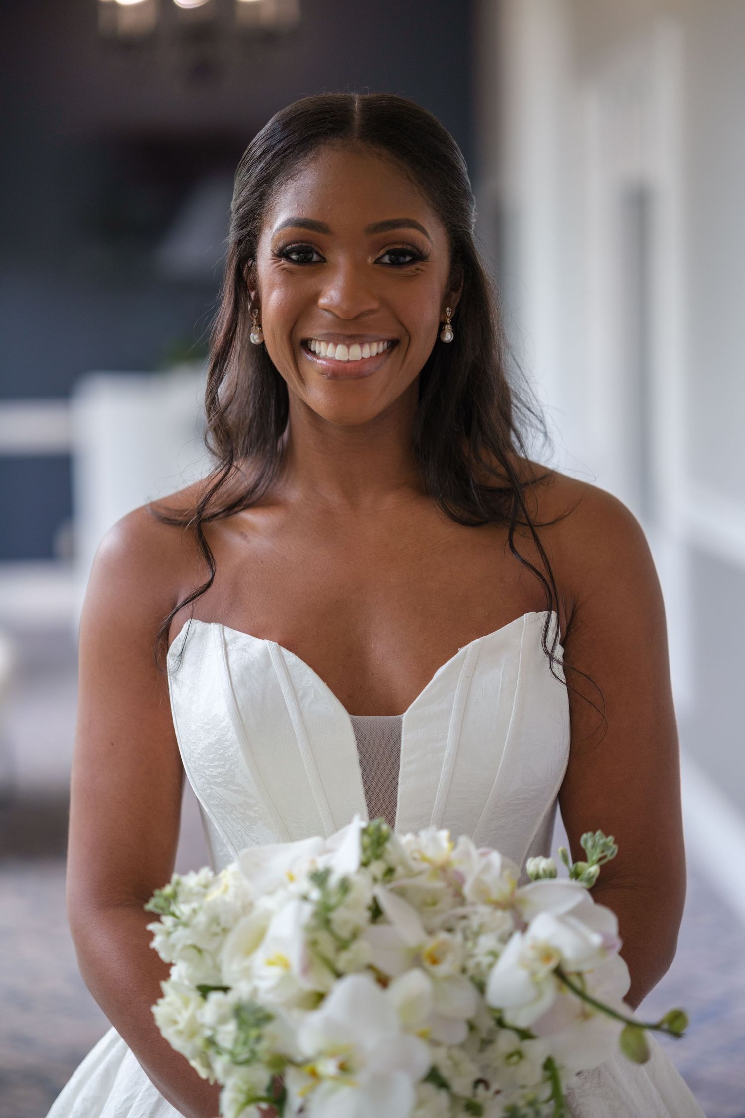 Smiling Black bride in strapless white gown holding white floral bouquet on her wedding day.