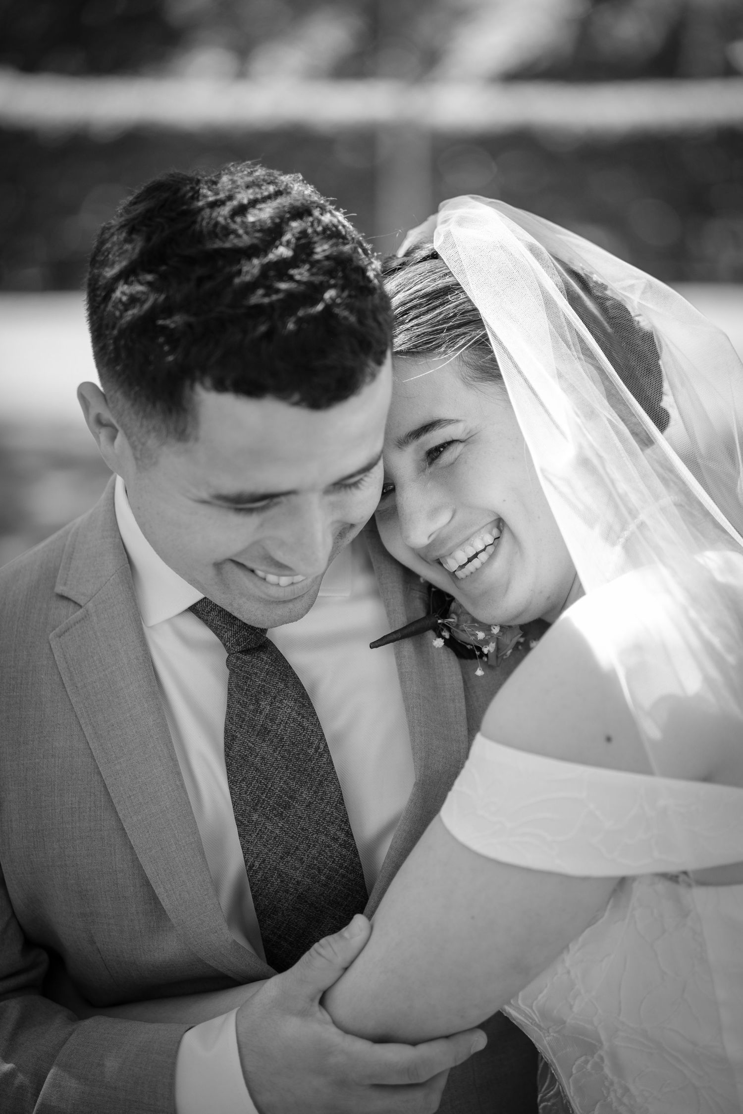 A smiling bride and groom share a joyful embrace in a black and white wedding photo.