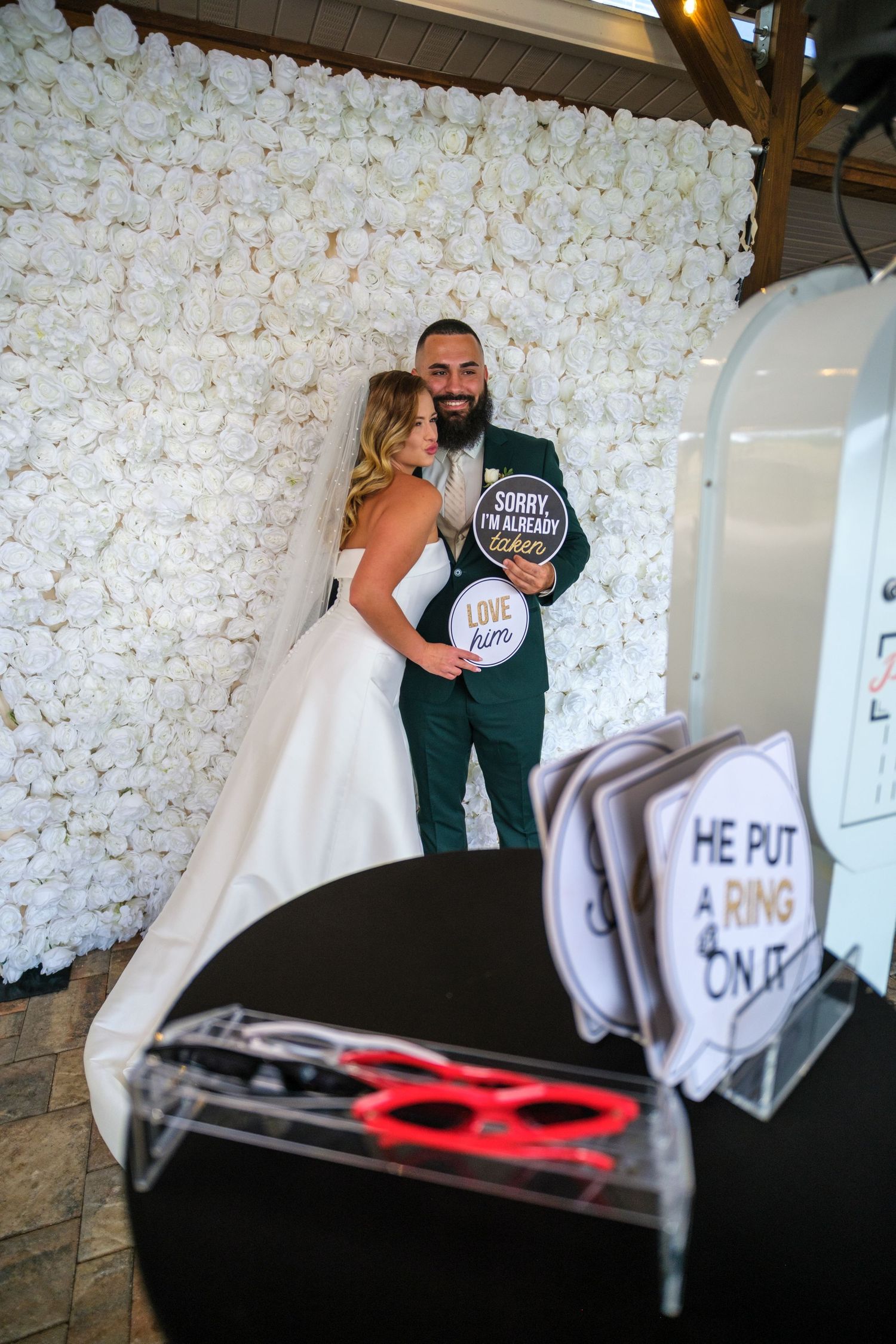 A series of wedding photos showing a white floral backdrop wall with signs and decorative elements at a reception venue.