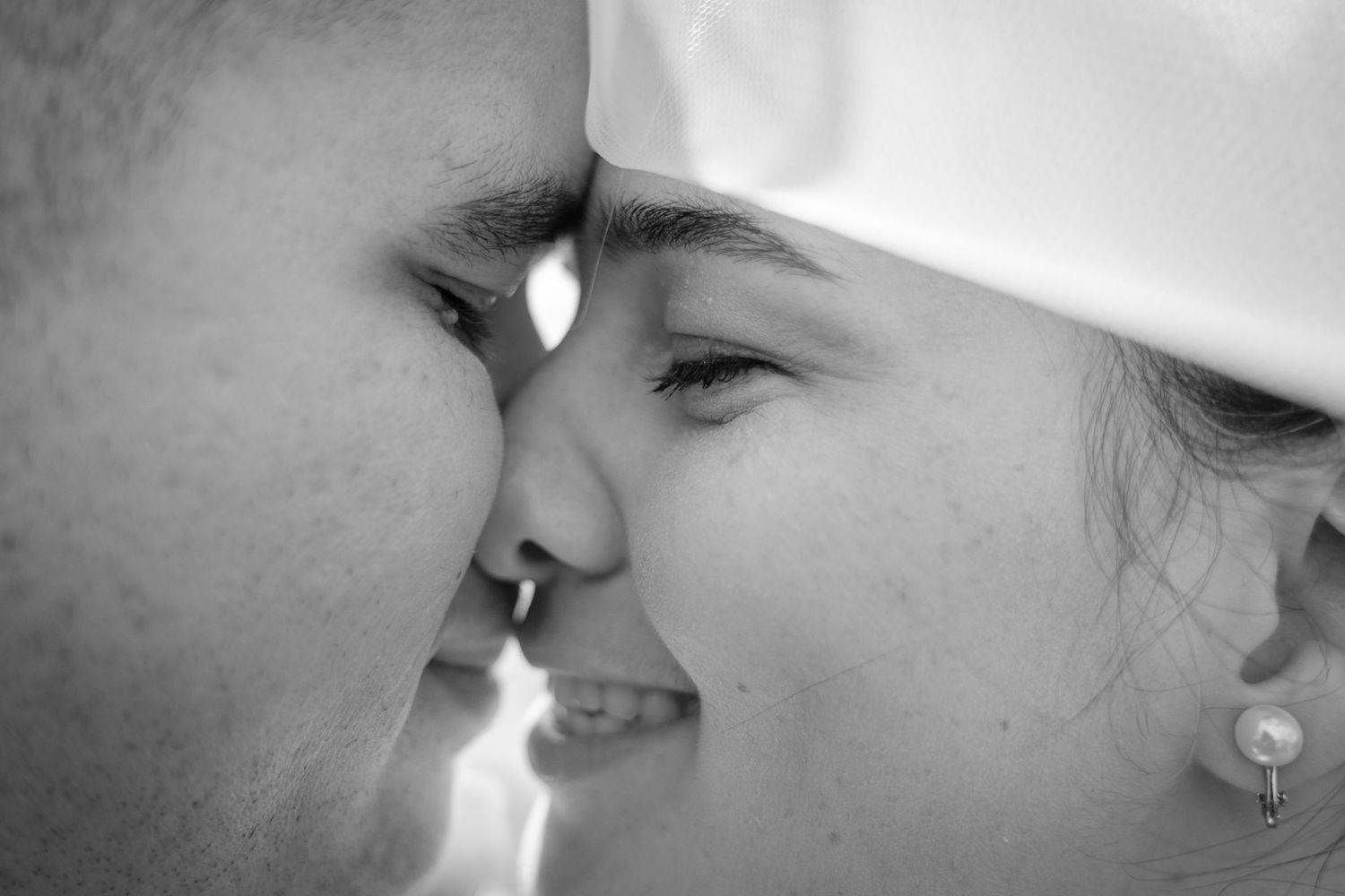 Black and white close-up of a couple sharing a romantic moment, foreheads touching and smiling.