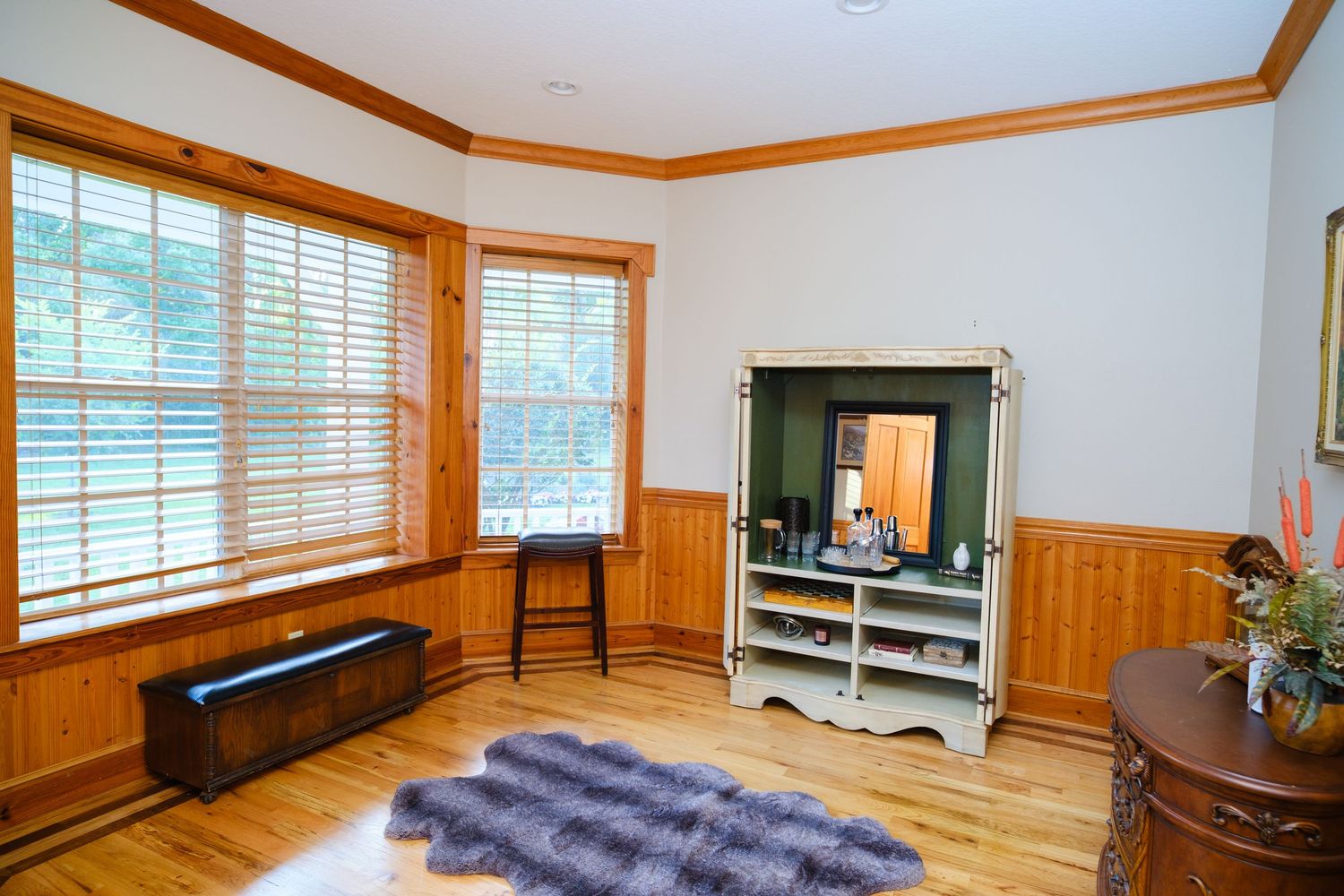 Bright corner room with wood trim, windows with blinds, entertainment center, and hardwood flooring.