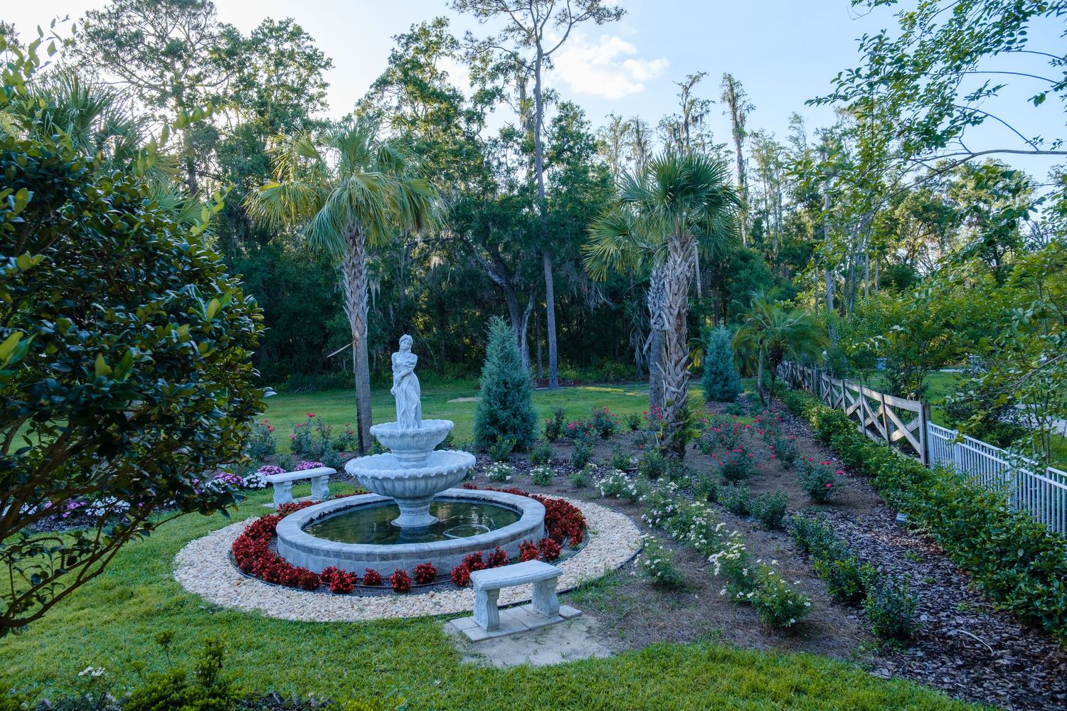 A serene garden fountain surrounded by red flowers and landscaping in a circular design at dusk.