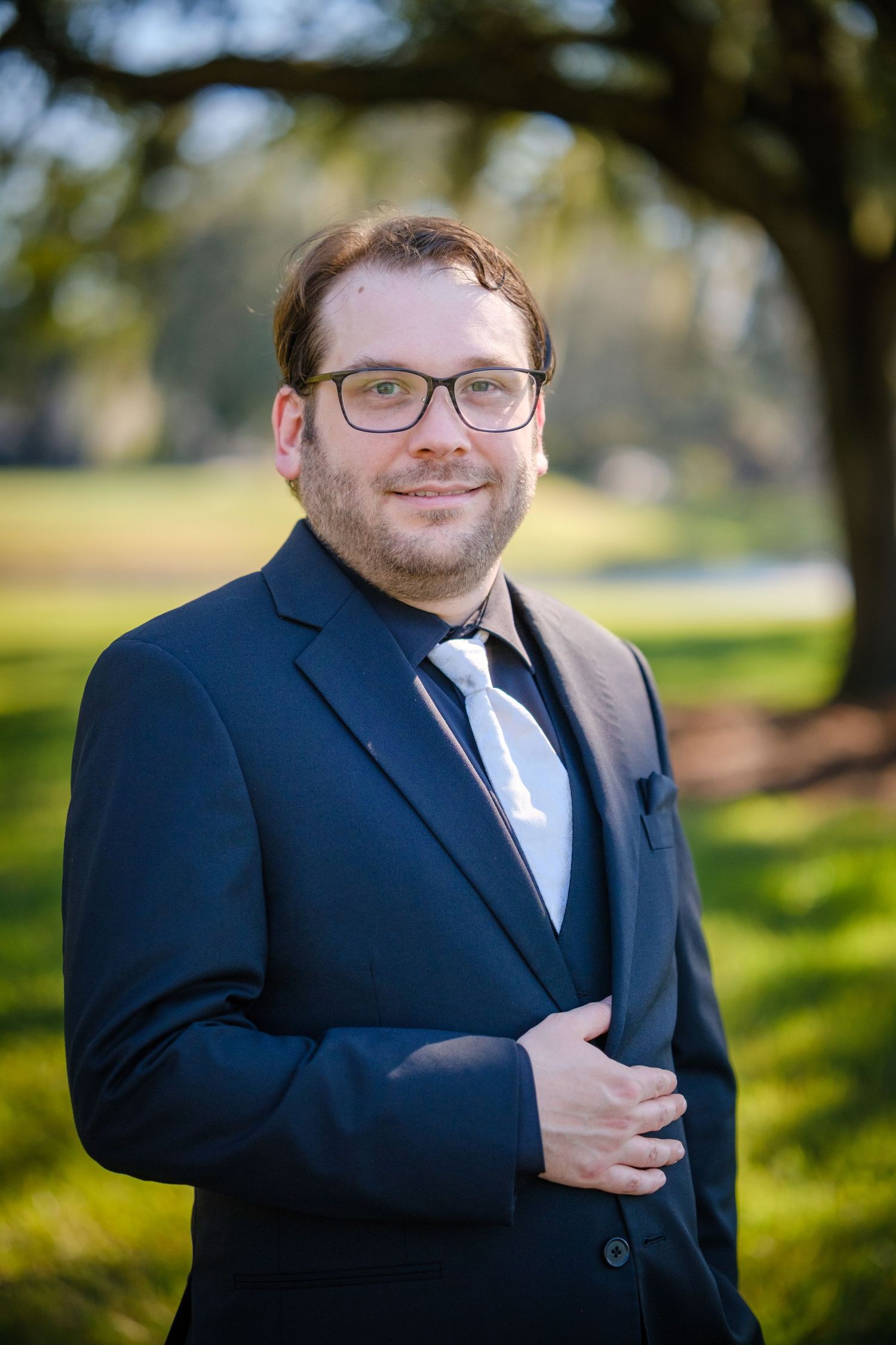 A person wearing a navy suit and glasses poses outdoors in a series of professional portrait shots.