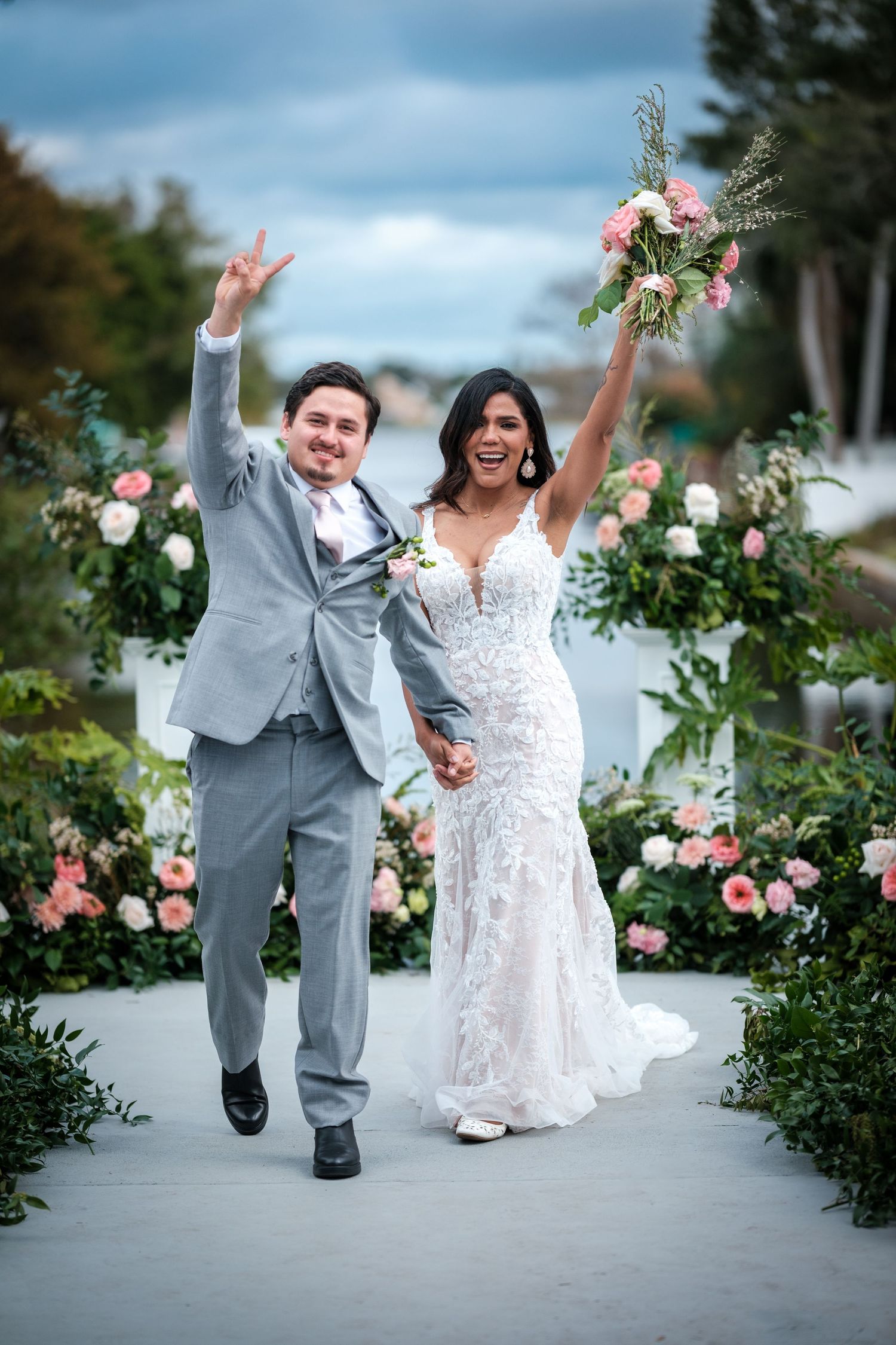 Joyful wedding couple dancing and celebrating on a pathway lined with pink roses.