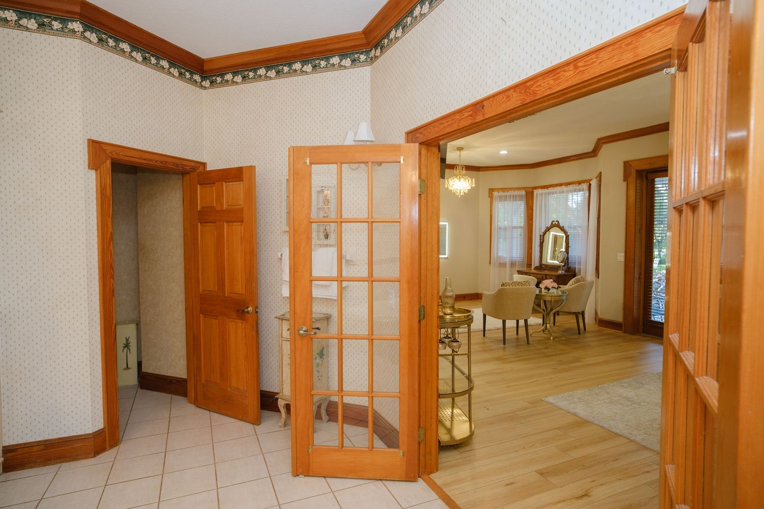 Interior view of home entrance with wooden French doors, ornate crown molding, and tile flooring leading to dining area.