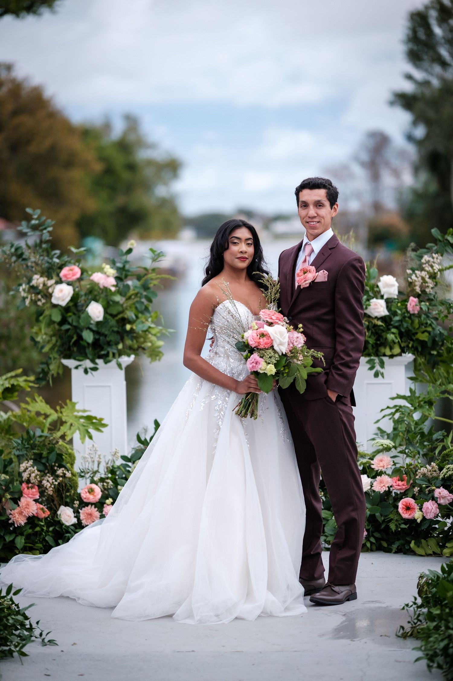 Wedding couple poses in garden setting surrounded by pink and white roses.