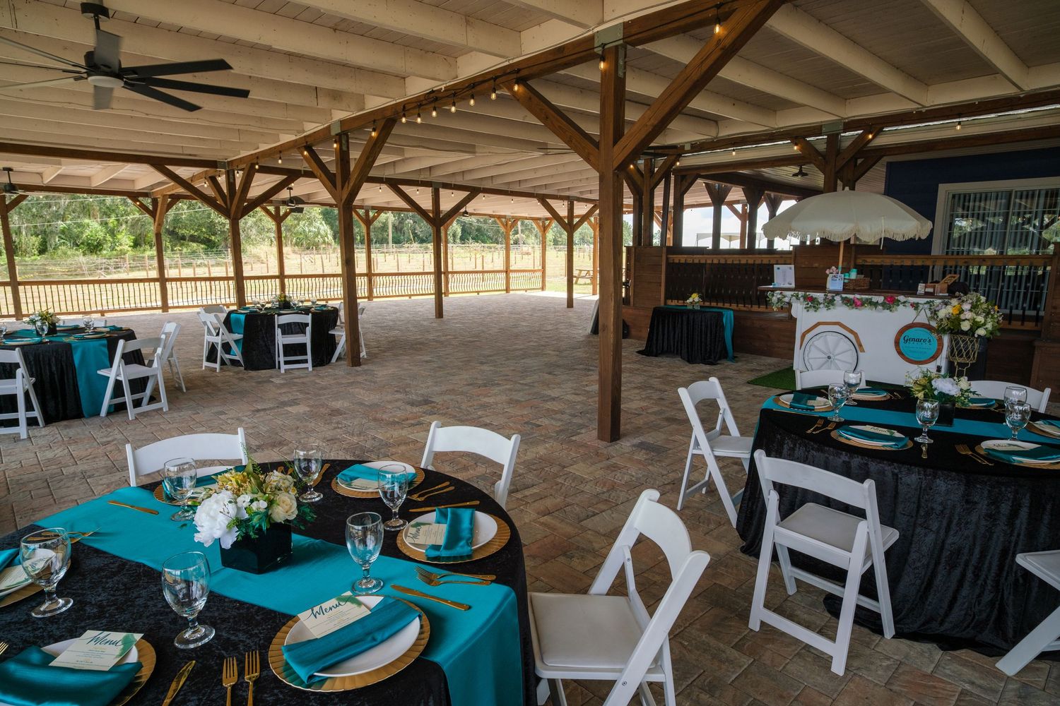 Rustic outdoor pavilion with wooden beams and teal and black wedding reception table settings.