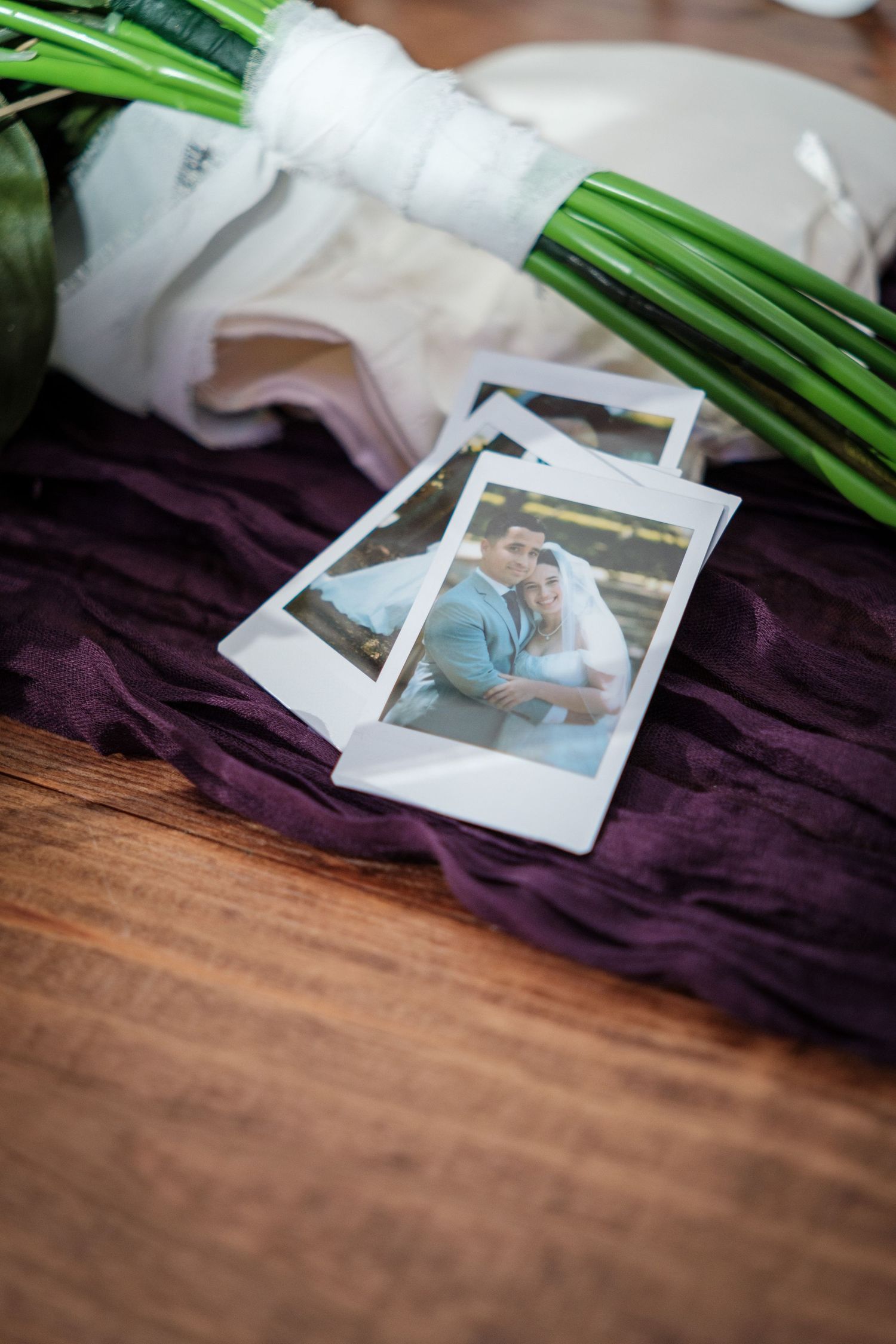 Polaroid wedding photos of couple on purple fabric beside green-stemmed bridal bouquet.