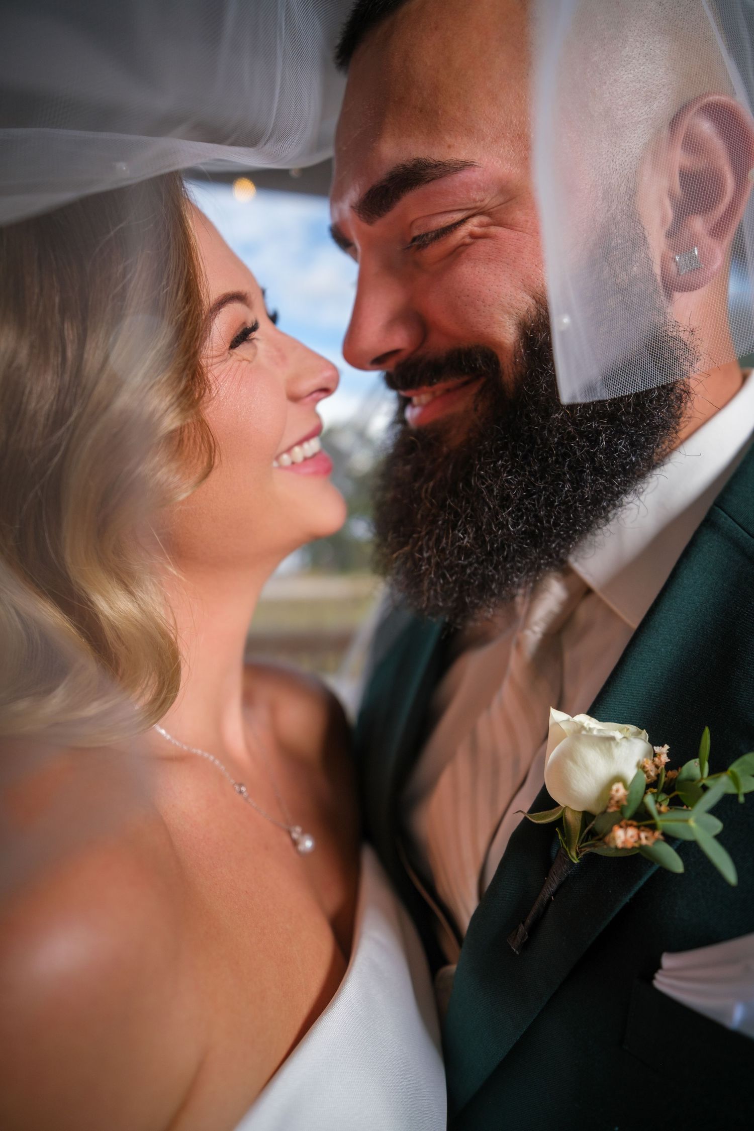 Romantic close-up wedding photos showing tender moments between a bride and groom with a dark beard in a green suit.