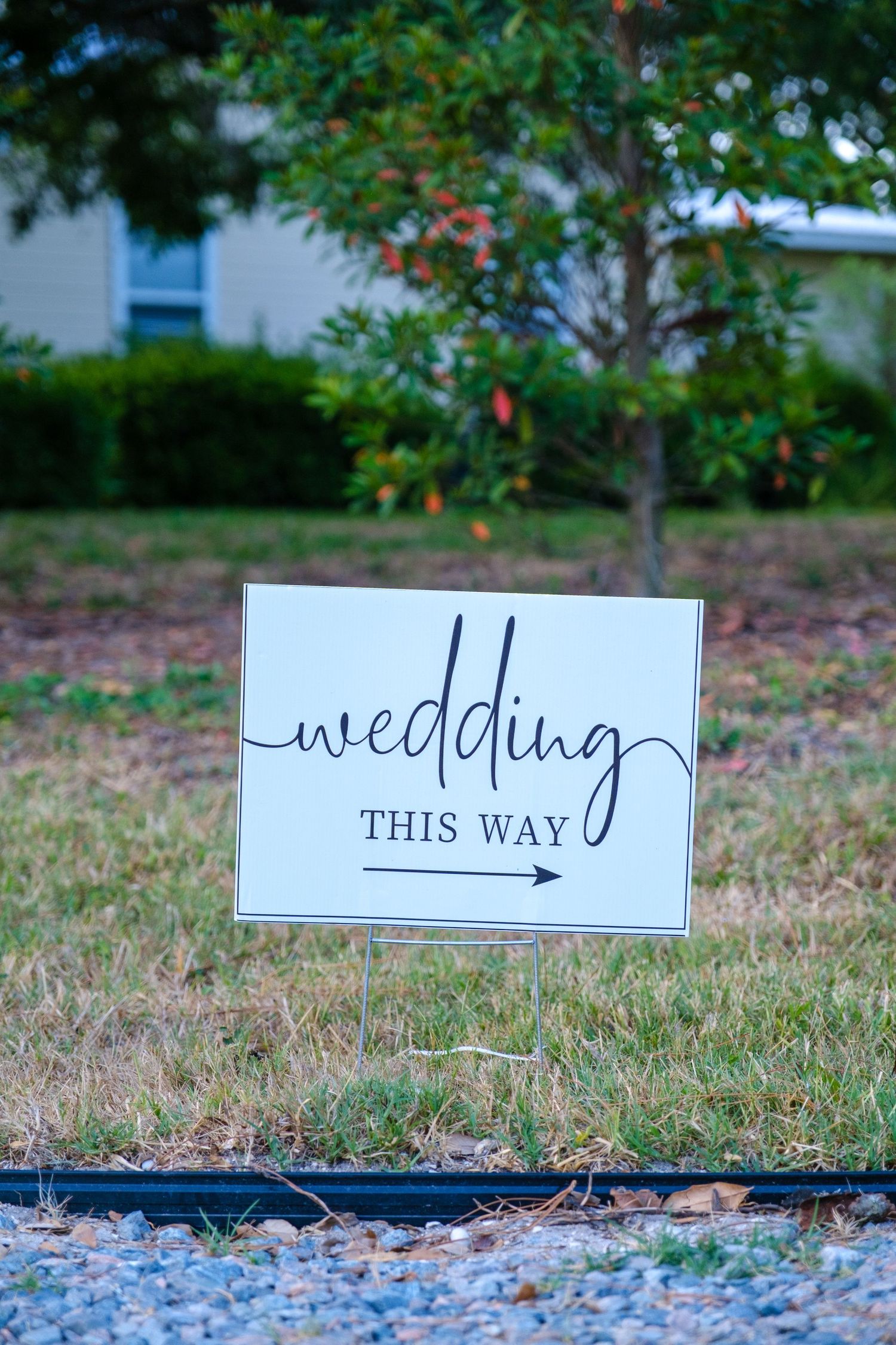 A rustic directional wedding sign with modern calligraphy and an arrow points the way on grassy ground.