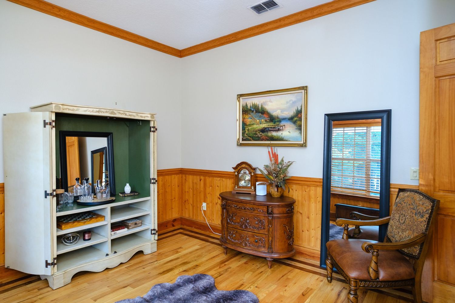 Interior room with wooden floors, wainscoting, vintage furniture, and TV armoire featuring classic decor and crown molding.