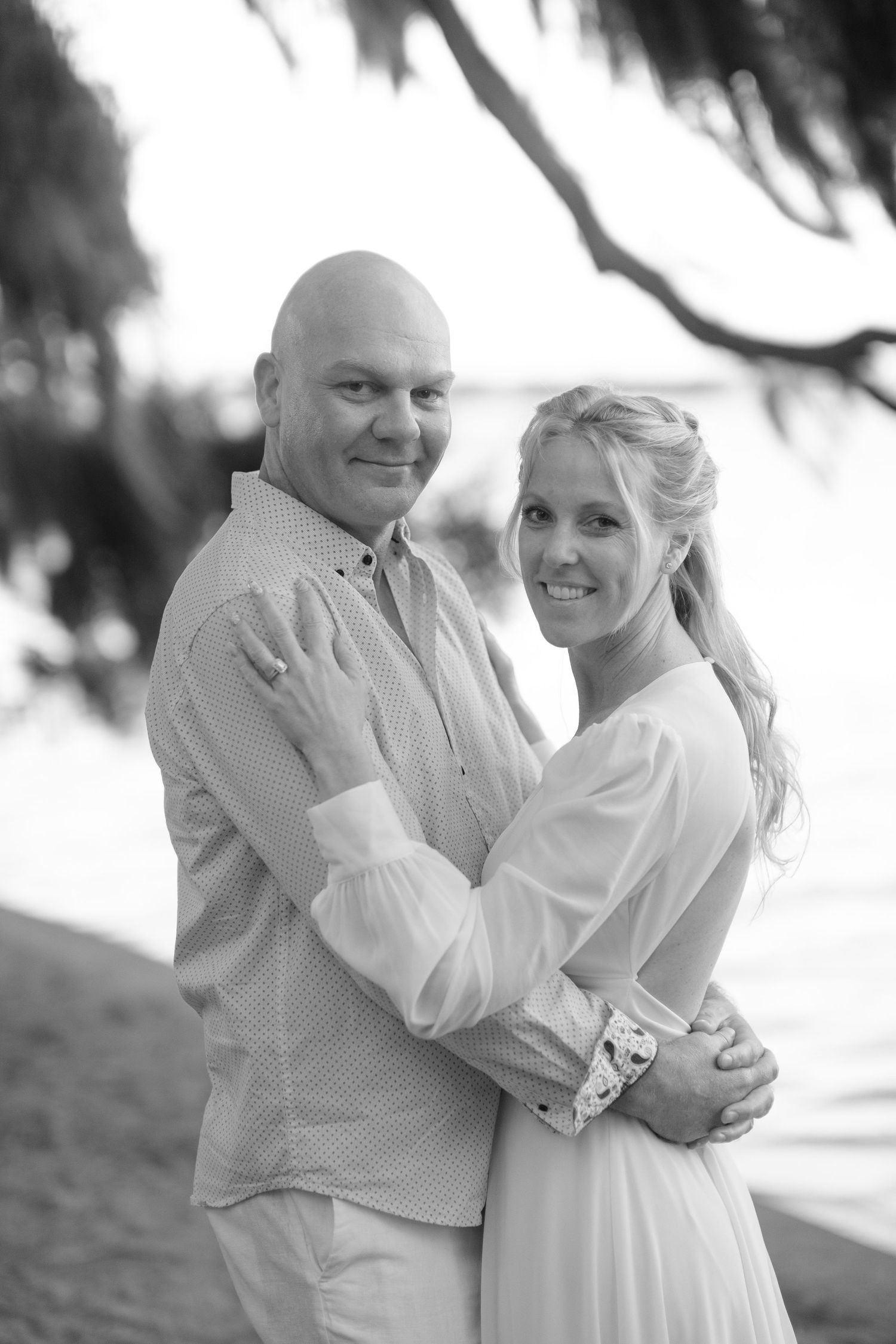 A couple in white clothing embraces and laughs together during a romantic outdoor photo session.