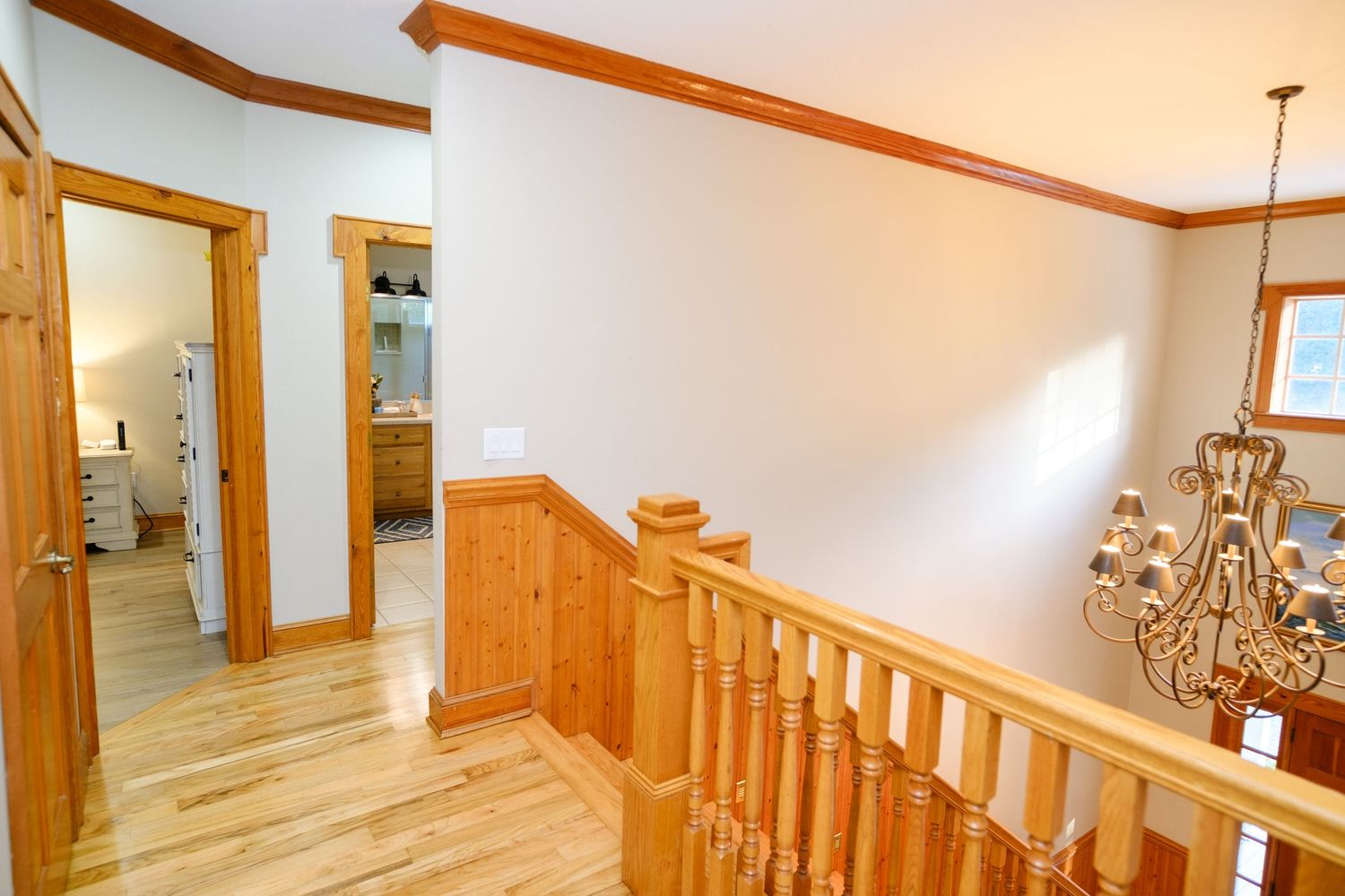Upstairs hallway with wood railings, maple trim and hardwood floors illuminated by an elegant chandelier.